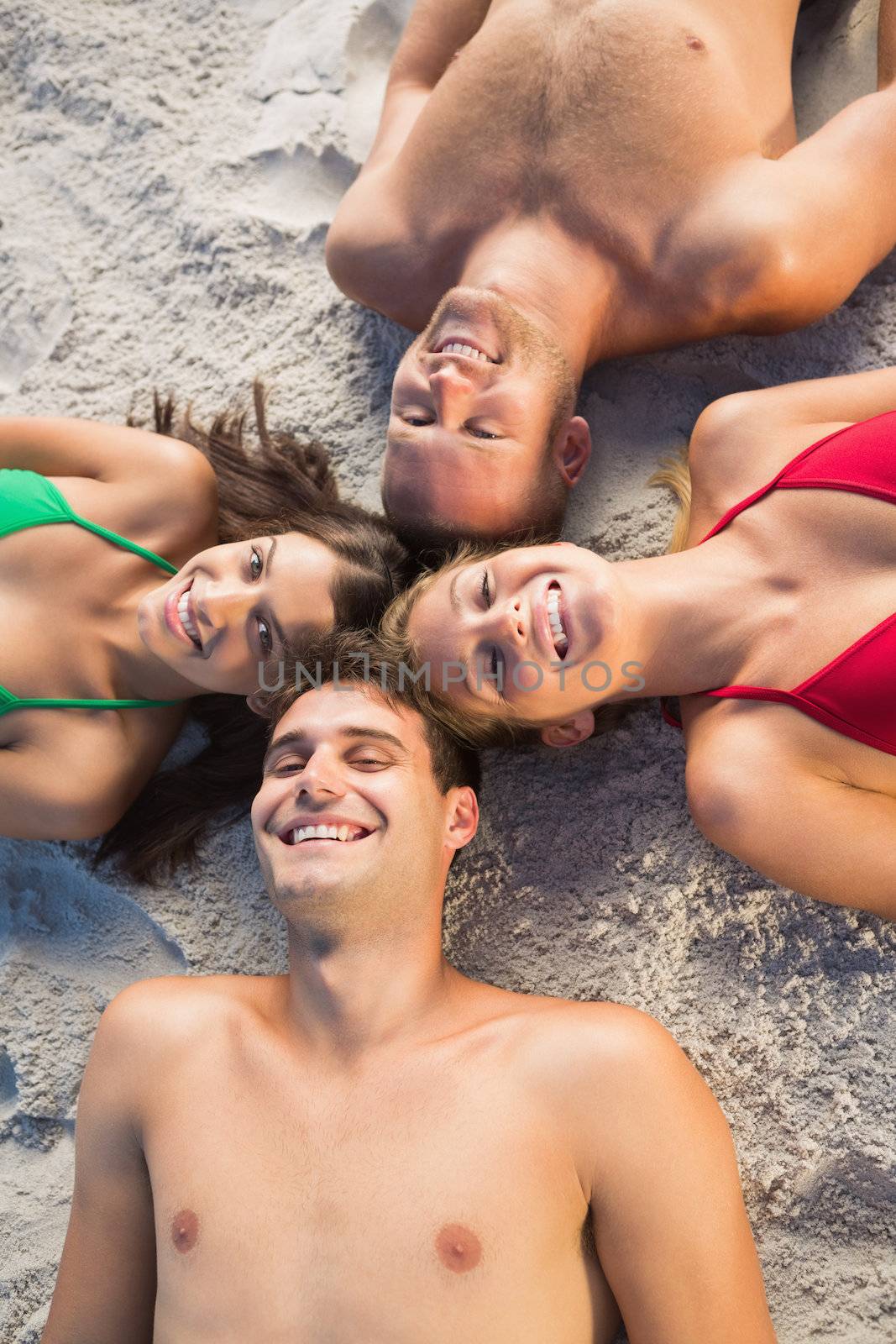 Overhead of smiling friends lying together in a circle on the beach