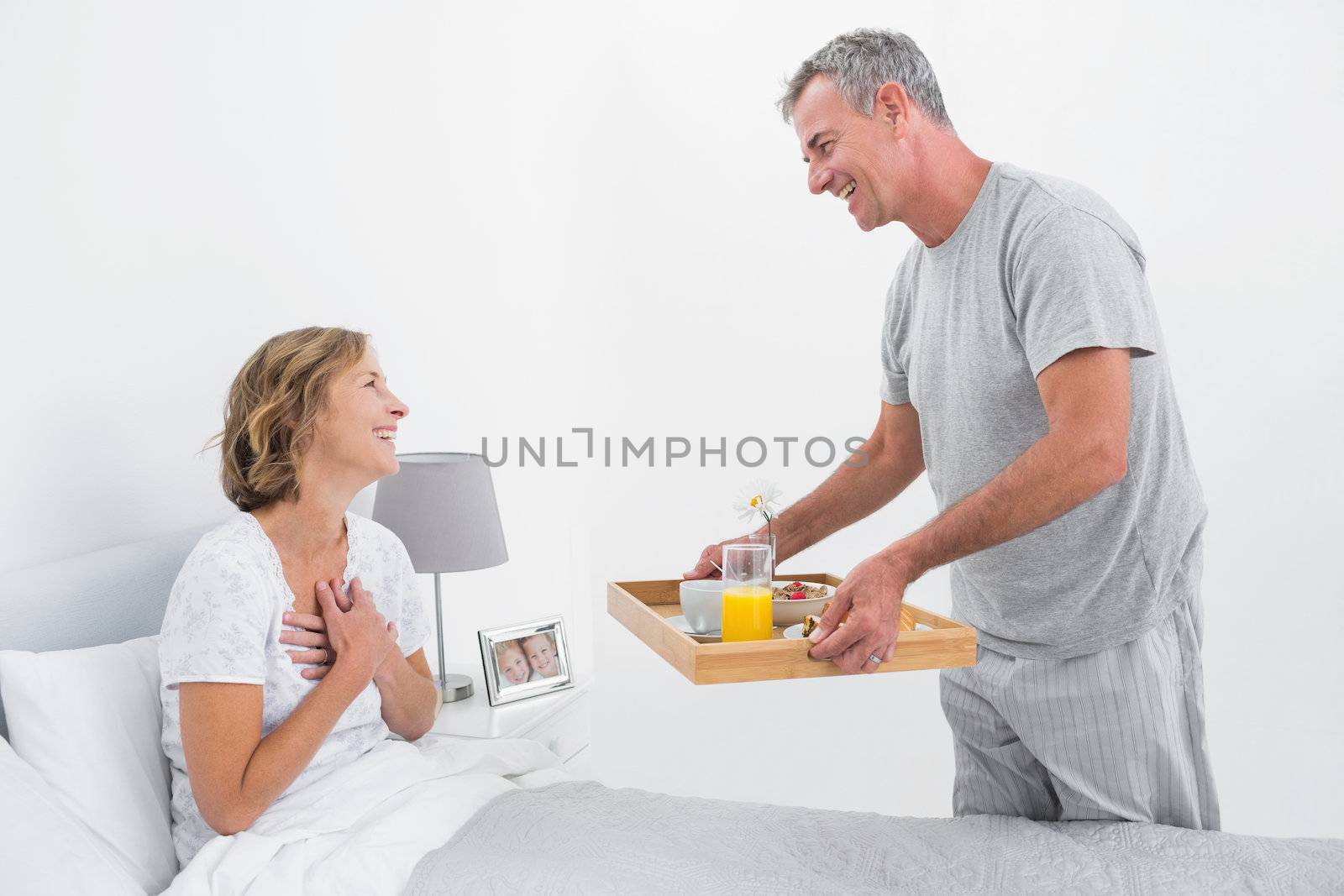 Loving husband bringing breakfast in bed to wife in bedroom at home
