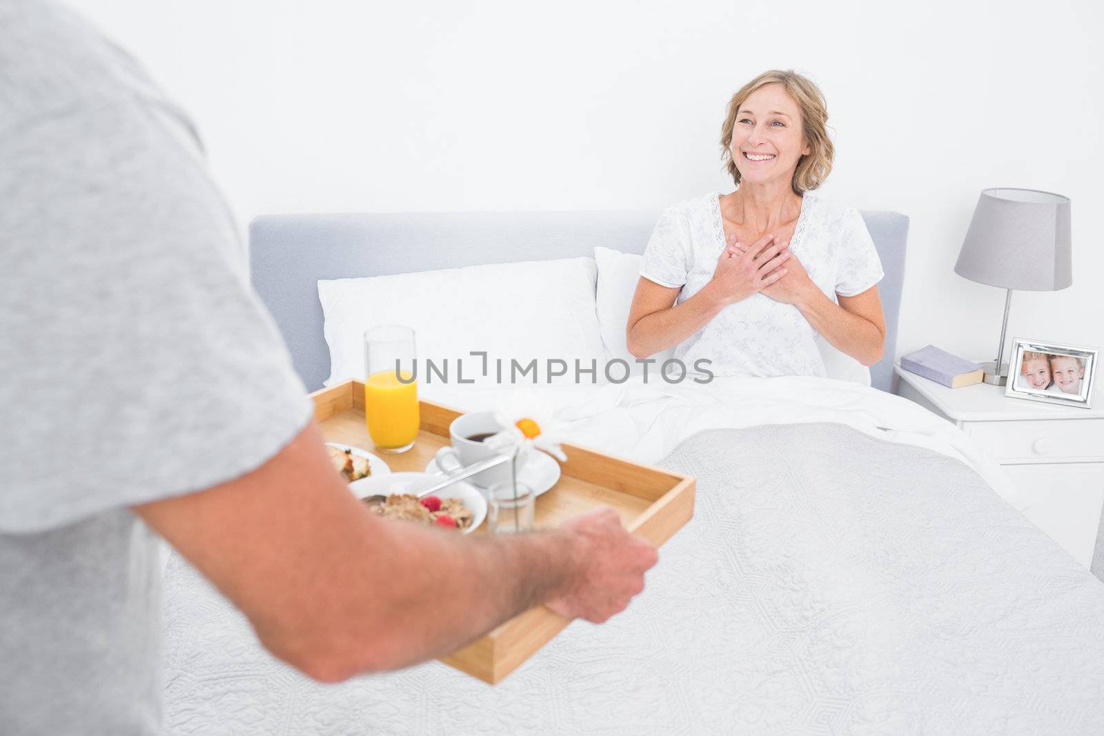 Husband bringing breakfast in bed to delighted wife in bedroom at home