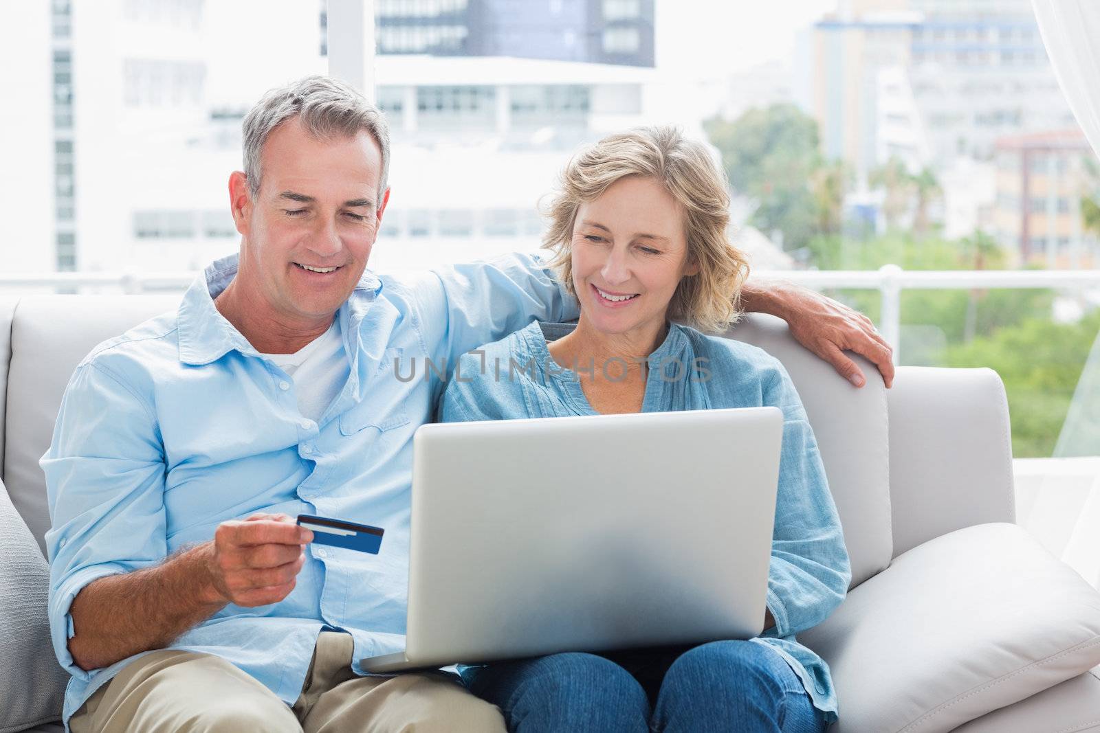 Smiling couple sitting on their couch using the laptop to buy online by Wavebreakmedia