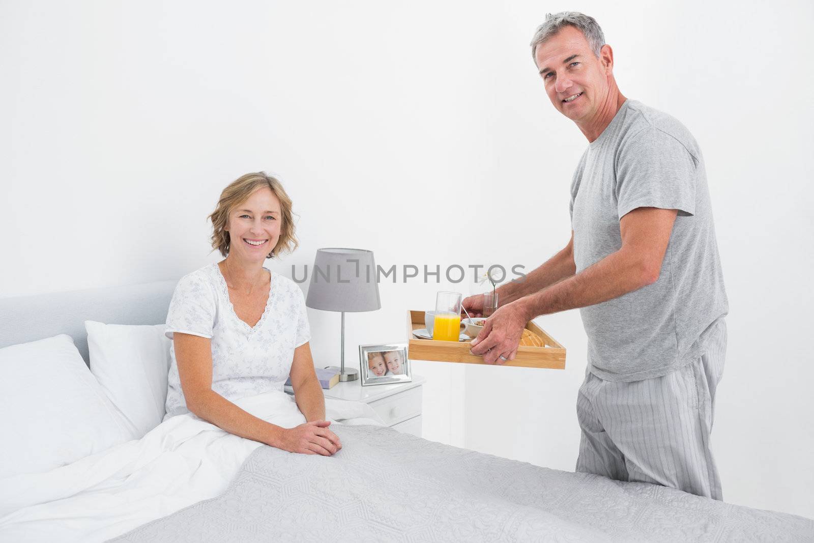 Happy husband bringing breakfast in bed to wife by Wavebreakmedia