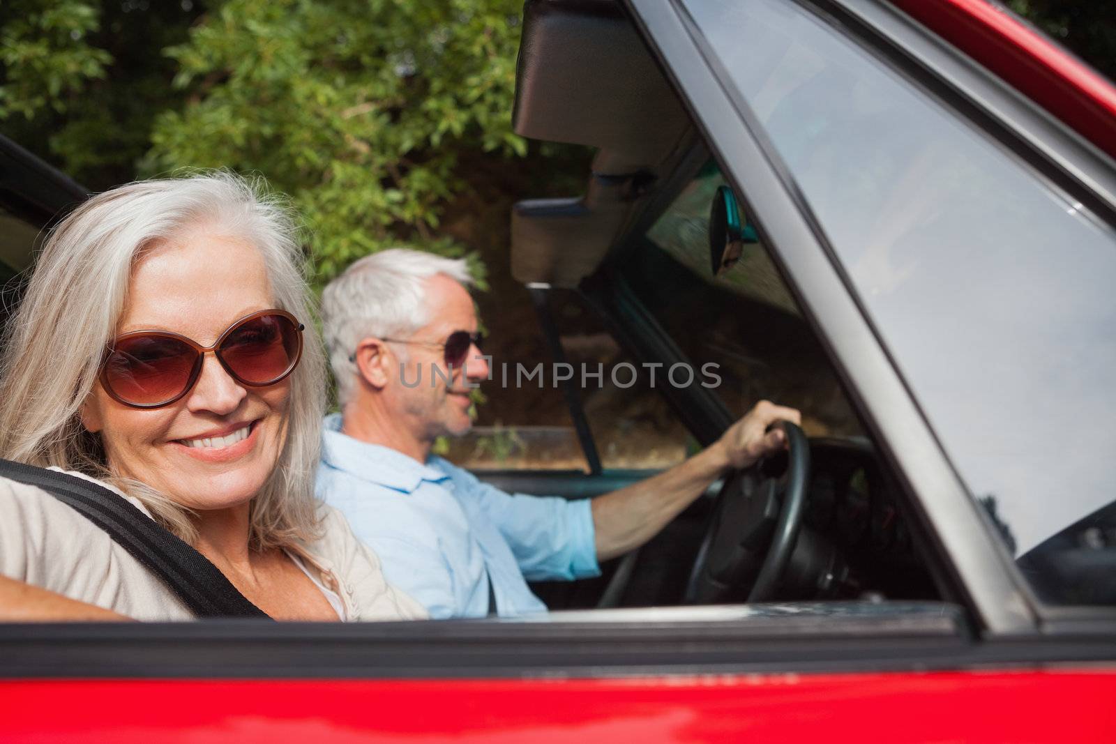 Side view of smiling mature couple driving red cabriolet on sunny day