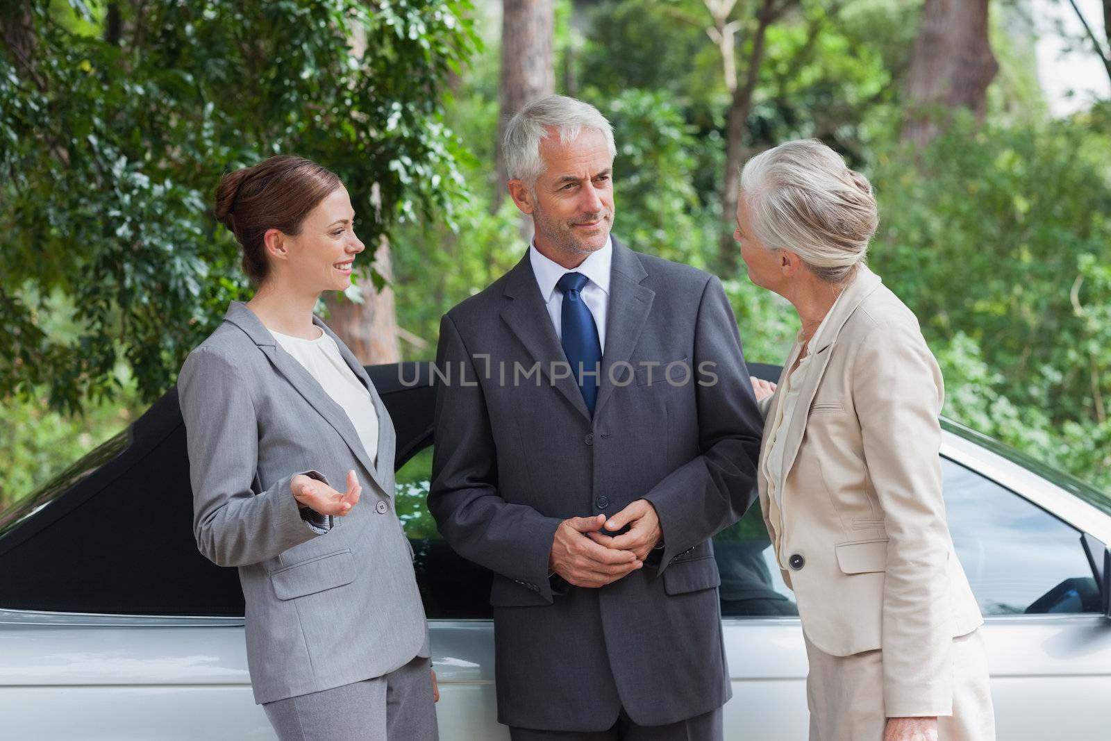 Smiling business people talking together by classy cabriolet on a bright day