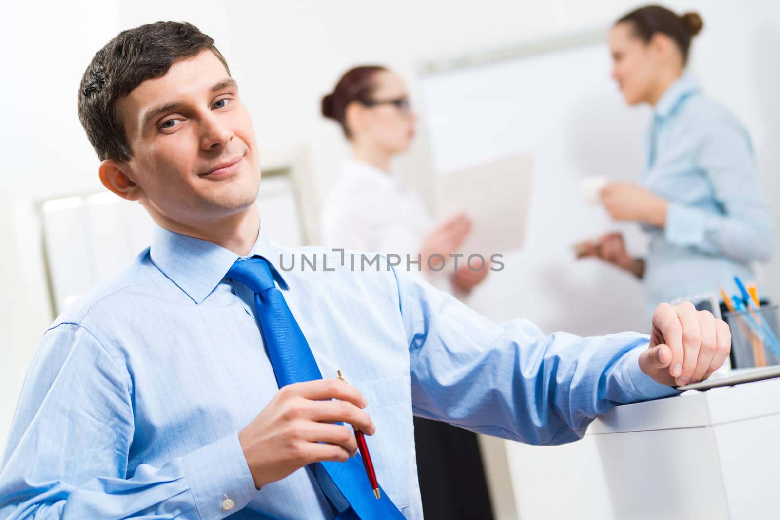 Portrait of a businessman in a blue shirt in the background of colleagues discussing