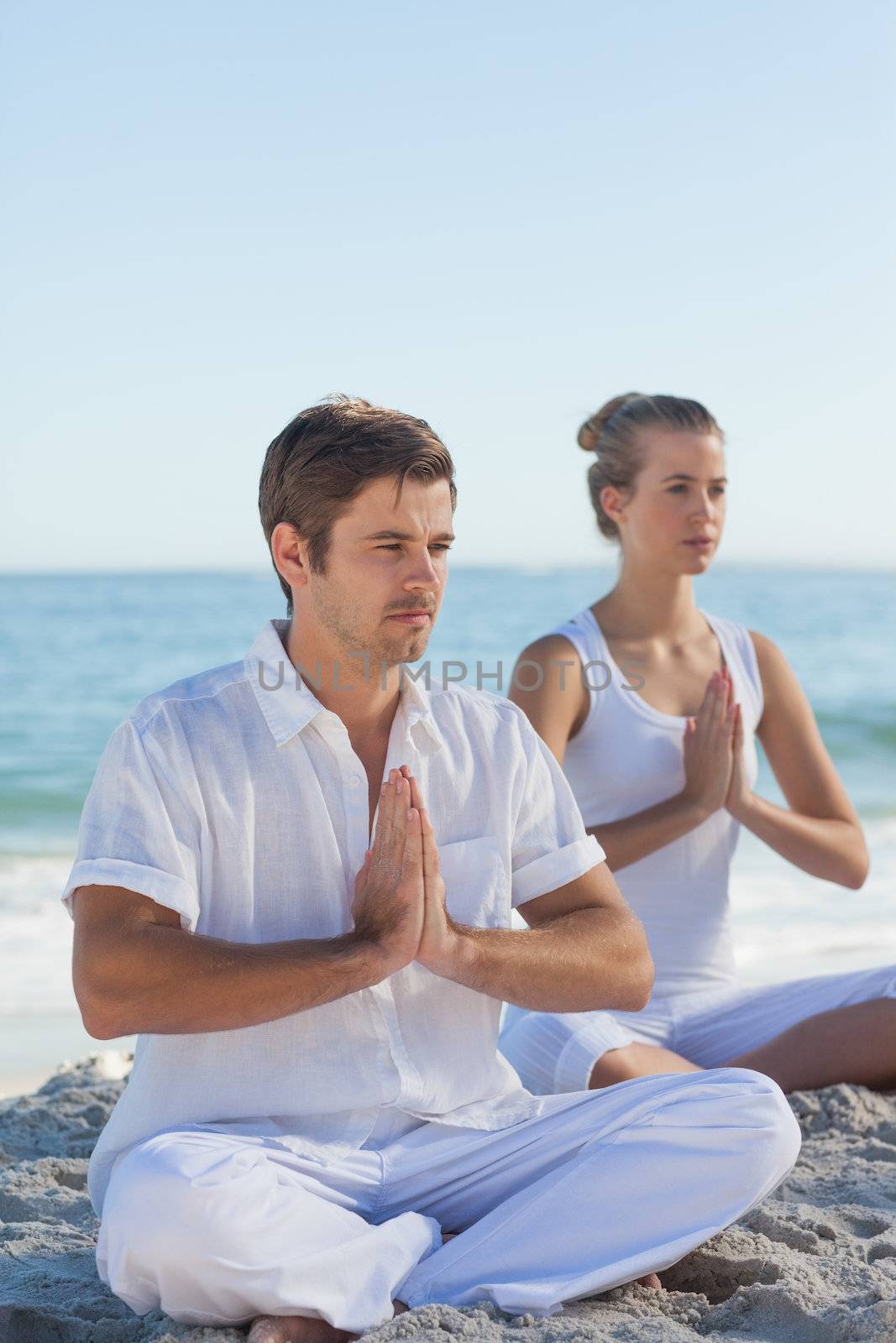 Man and woman practicing yoga on the beach on a sunny day