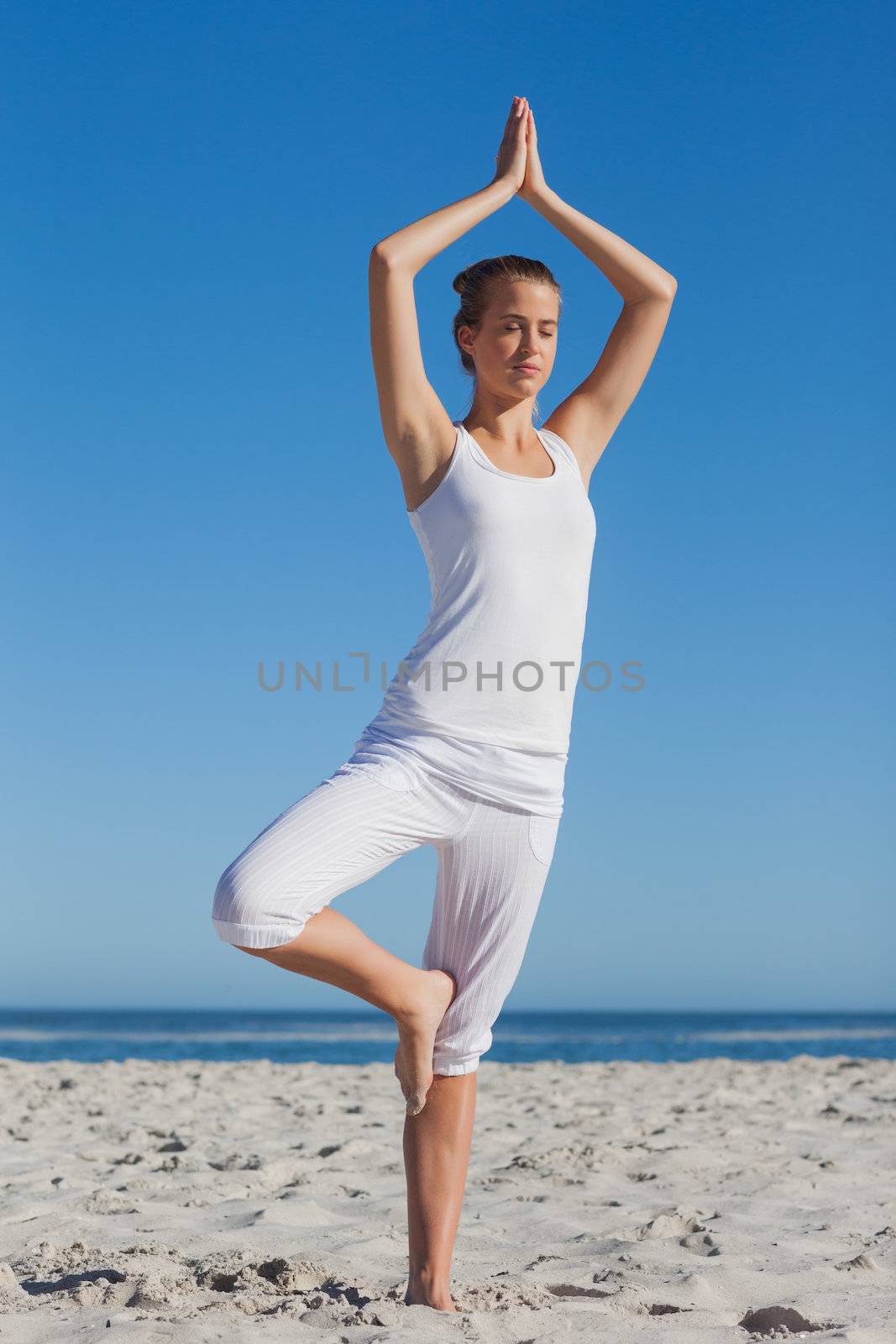 Woman in tree yoga pose at beach on a sunny day