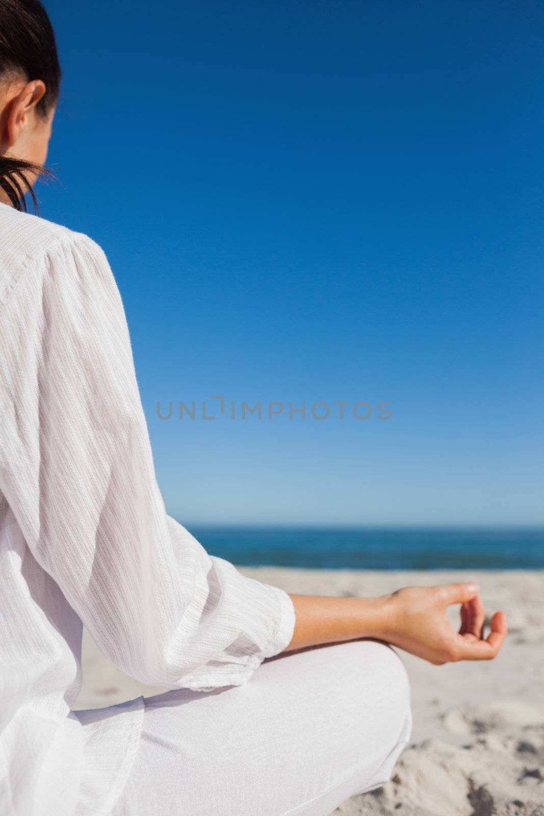 Brunette woman doing yoga at beach on a sunny day rear view