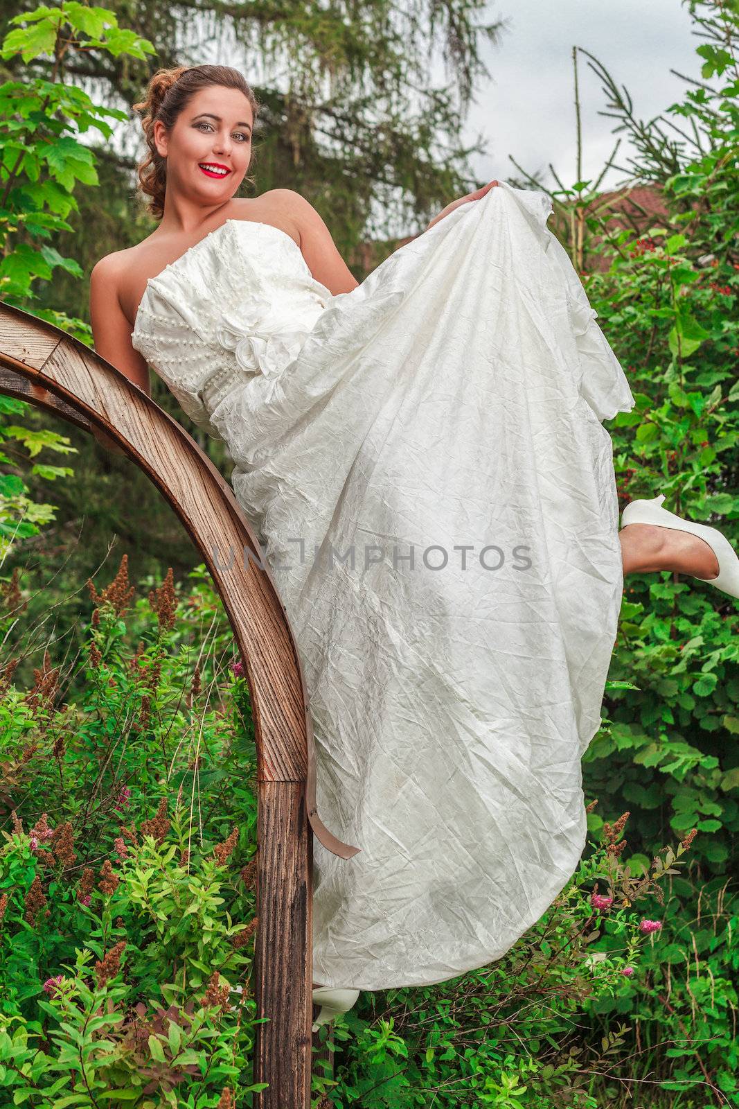Beautiful bride in her wedding gown posing in a lush green garden with a joyful smile on her face