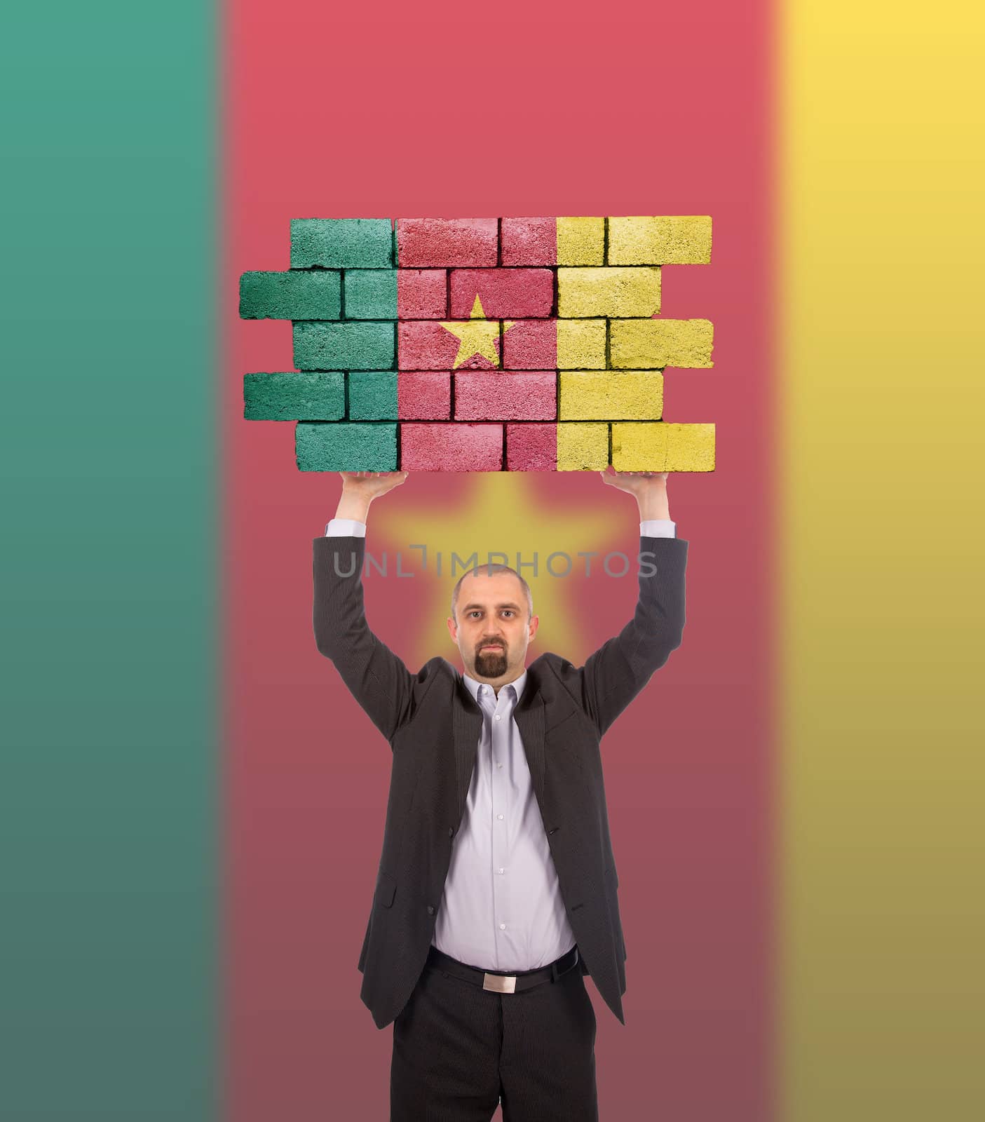 Businessman holding a large piece of a brick wall, flag of Cameroon, isolated on national flag