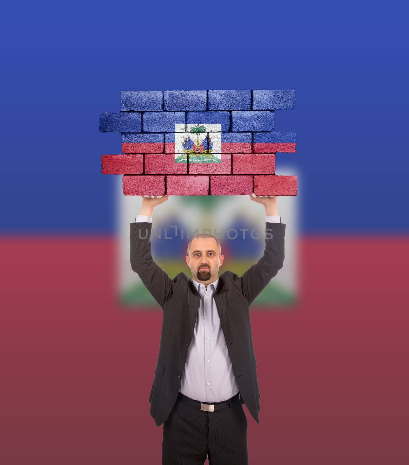 Businessman holding a large piece of a brick wall, flag of Haiti, isolated on national flag