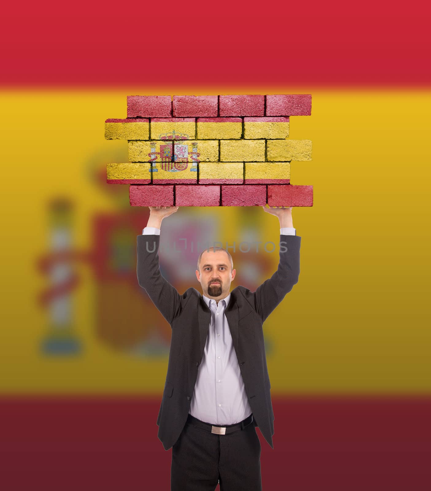 Businessman holding a large piece of a brick wall, flag of Spain, isolated on national flag