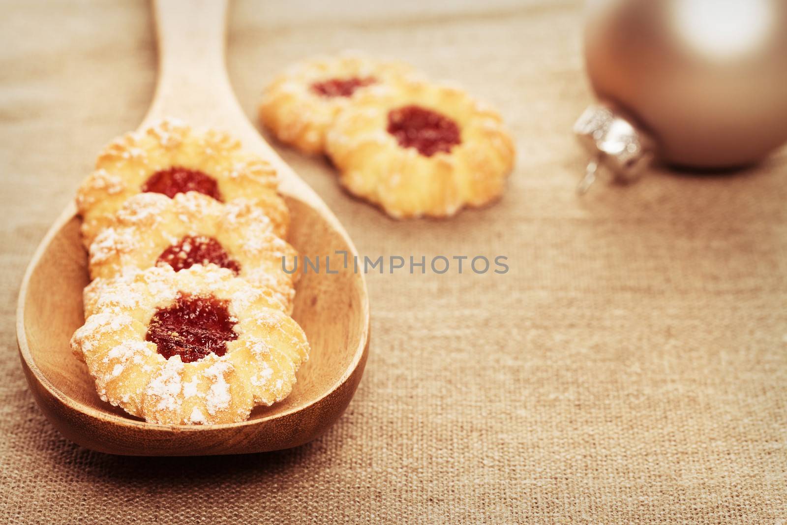 christmas cookies with jam on a vintage wooden spoon on linen fabric with a christmas ball in background