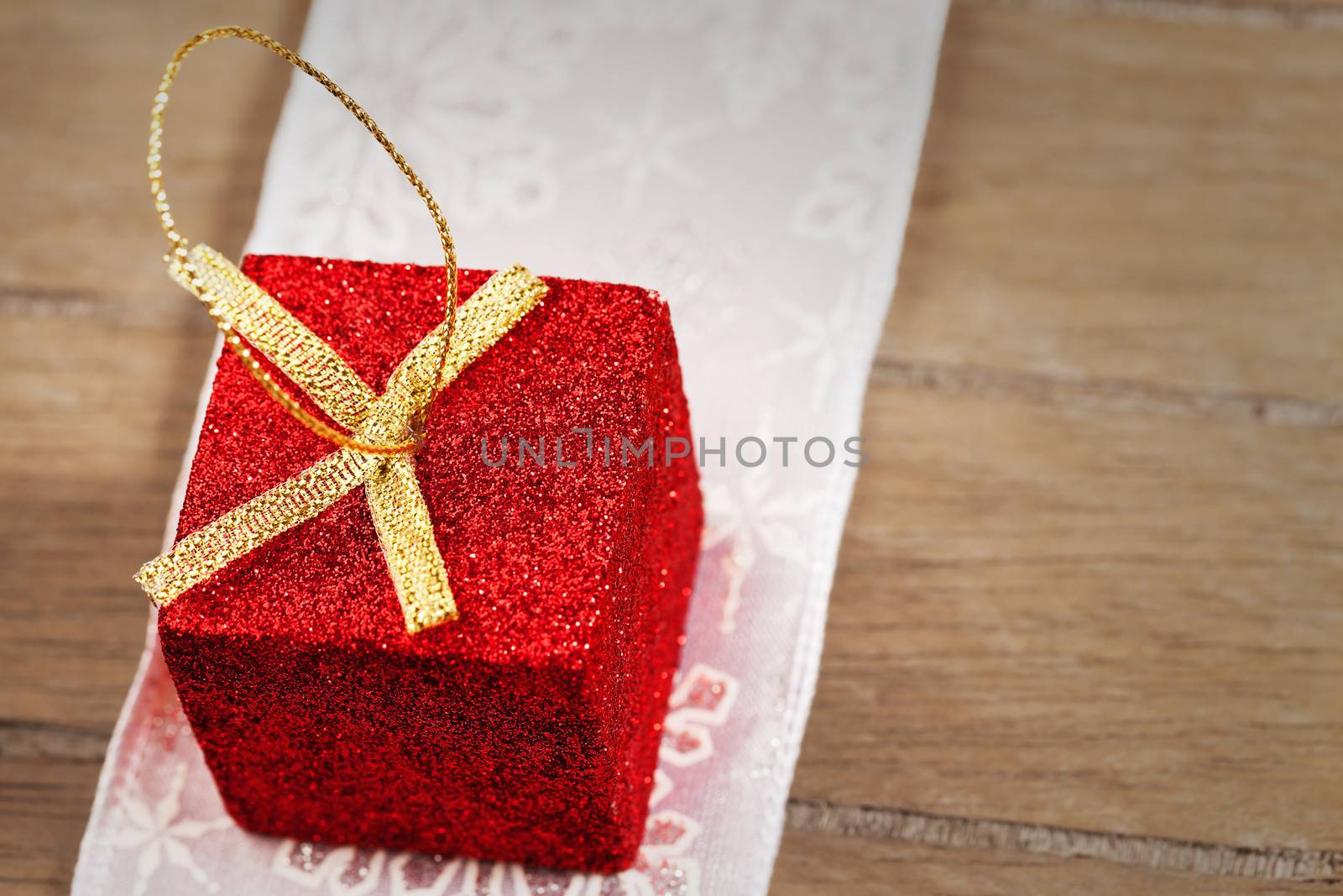 closeup of a red tiny glitter christmas present on a golden ribbon on wooden background