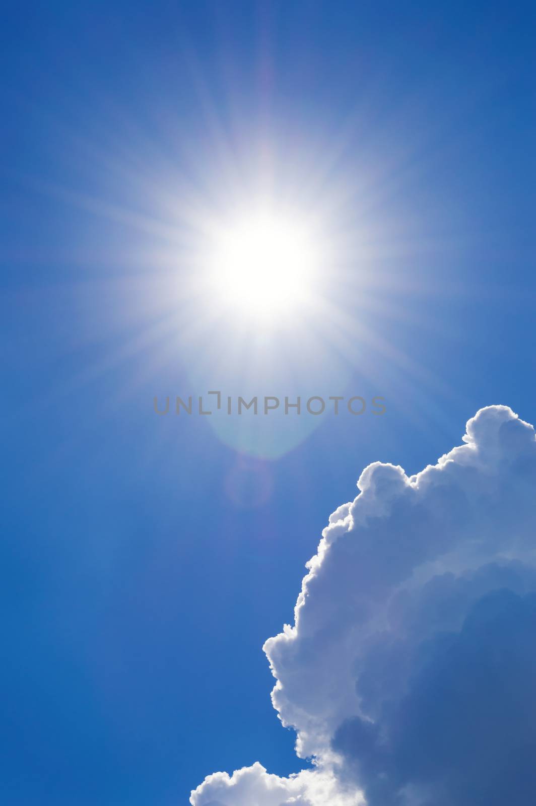 Shining sun at cloudy blue sky with lens flare, vertical shot