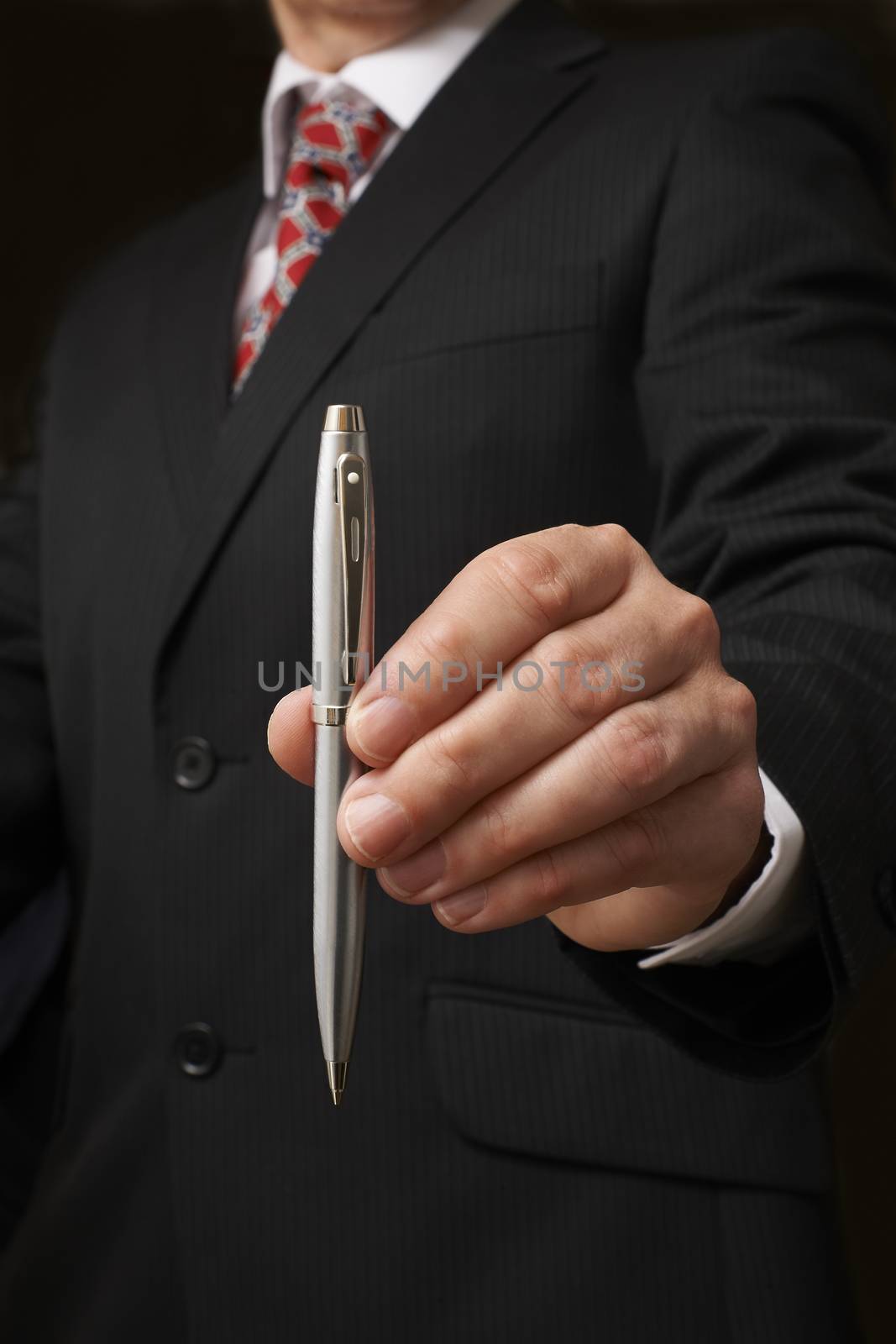 businessman in suit holding out pen towards camera