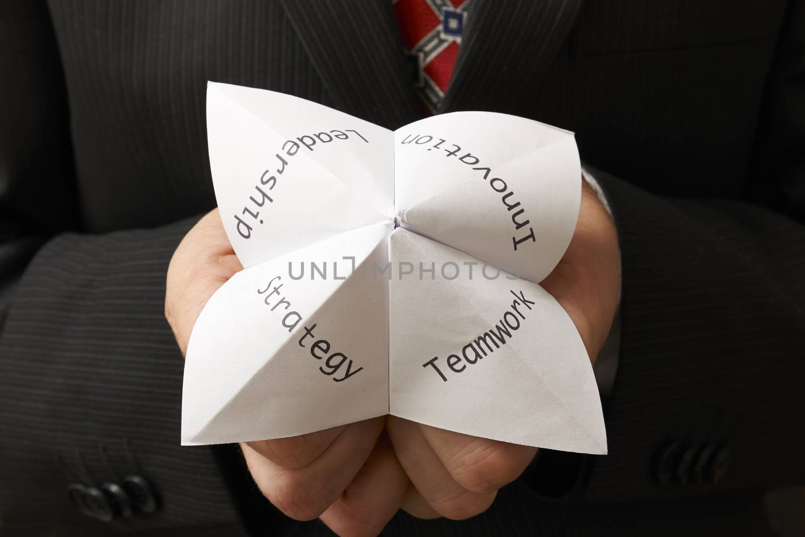 business man holding origami fortune teller with teamwork,leadership,innovation and strategy written on it