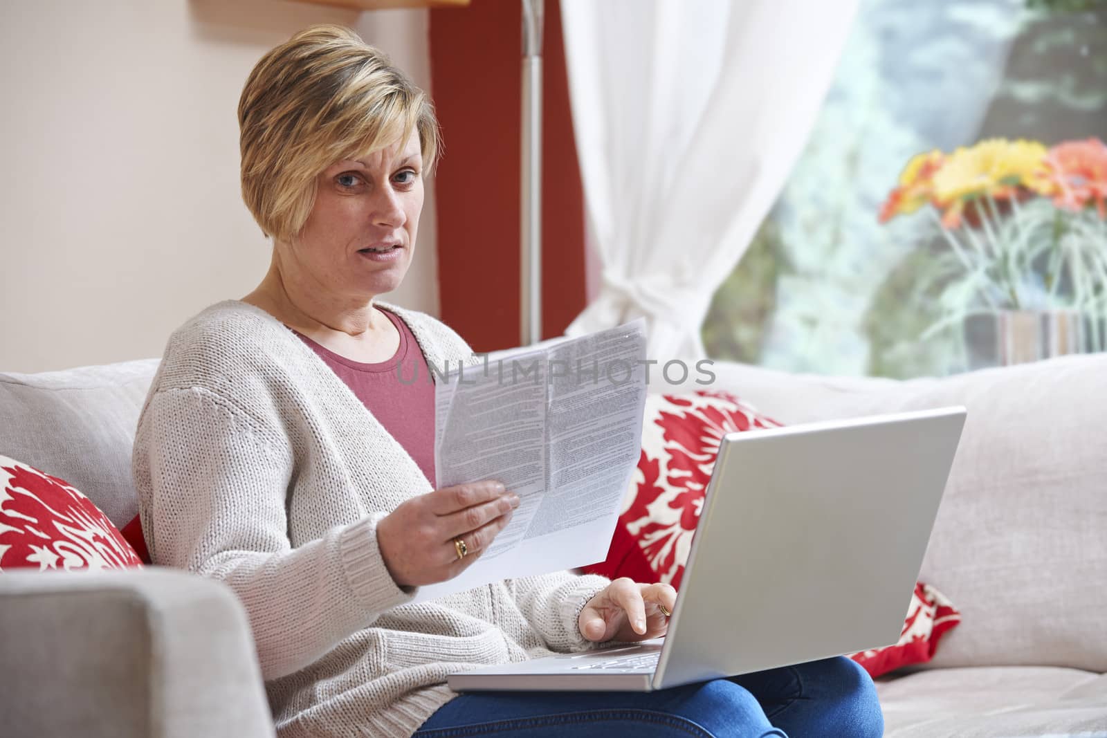  Woman sitting at home with laptop looking worried at camera while holding a bill