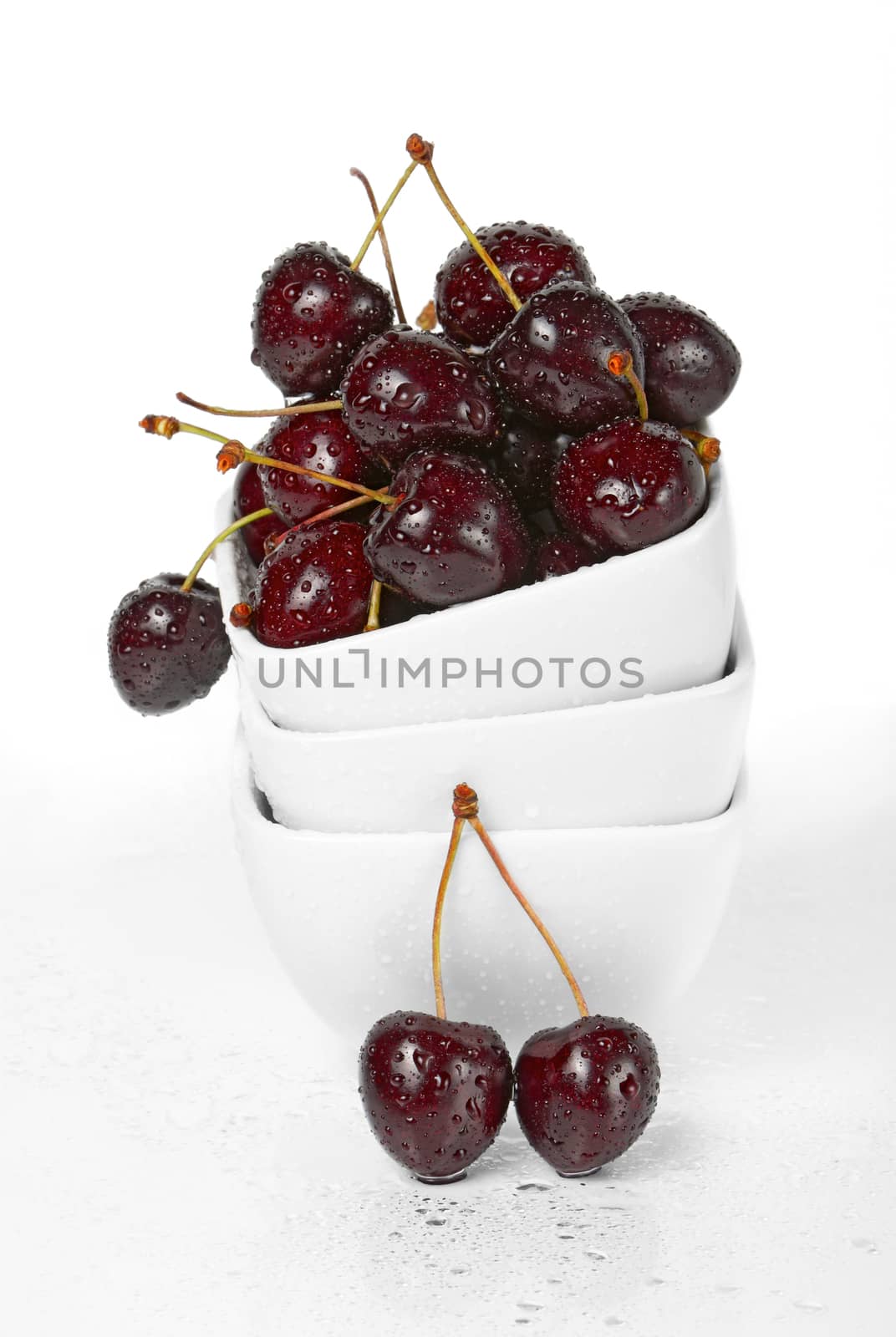 Fresh cherry berries in a stack of white ceramic bowls isolated on white background 