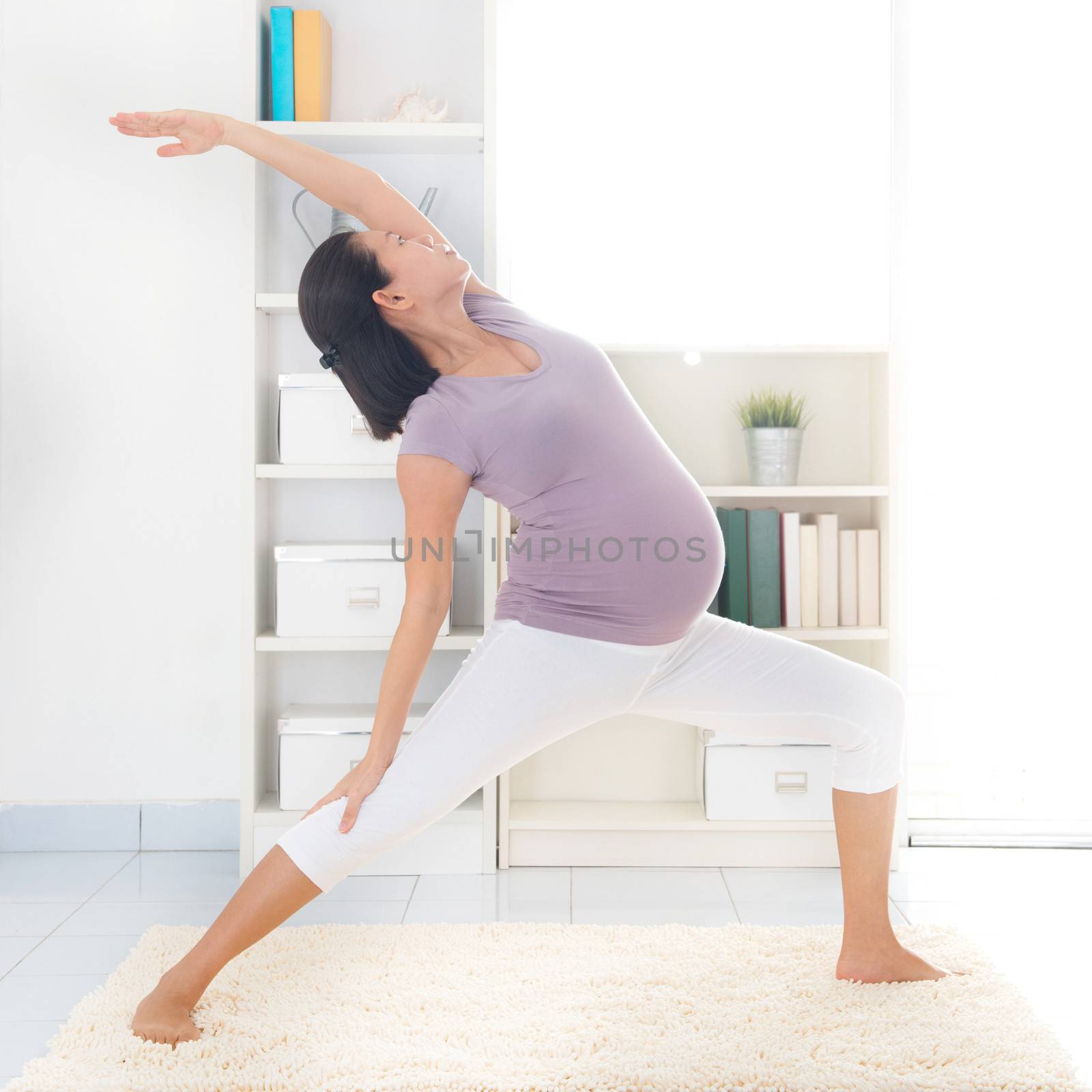 Prenatal yoga class. Full length healthy 8 months pregnant calm Asian woman meditating or doing yoga exercise at home. Relaxation and stretching.