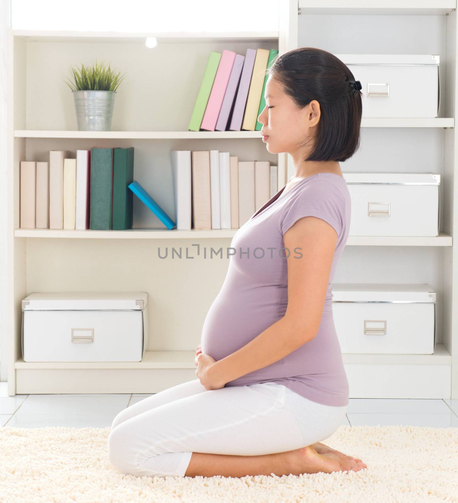 Prenatal yoga. Full length healthy 8 months pregnant calm Asian woman meditating home. Relaxation yoga hero pose.