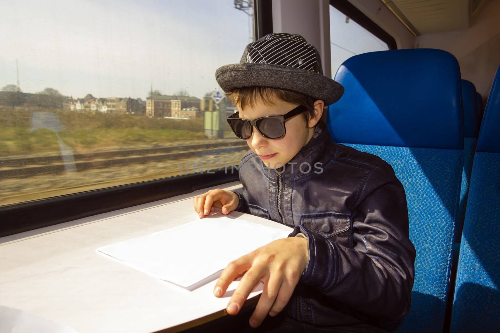 Handsome boy with sunglasses rides on a train reading from the paper