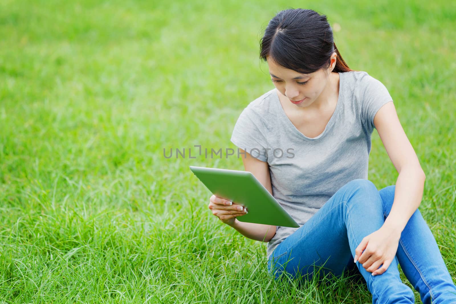 Woman sitting on grass with tablet computer by leungchopan