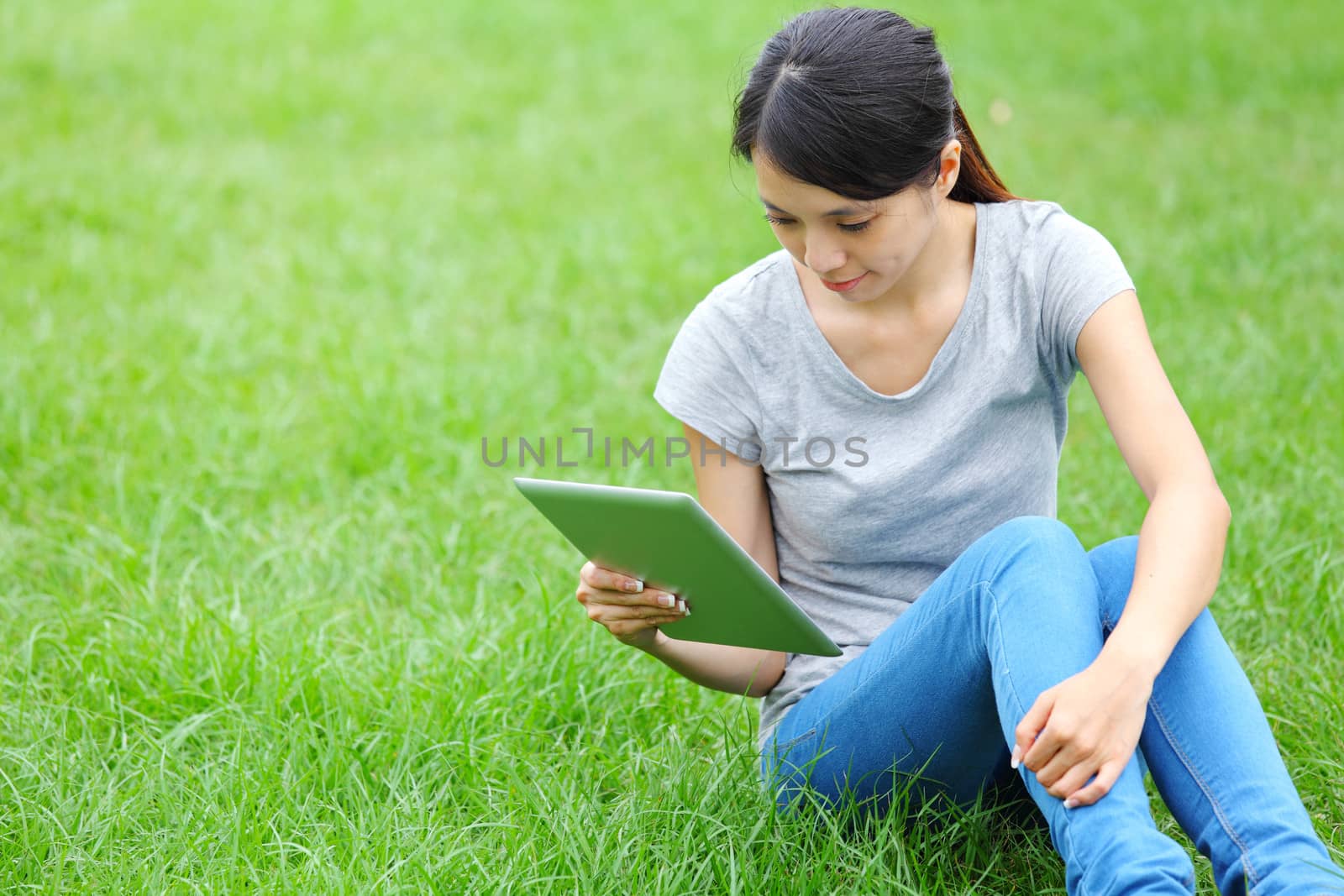 Woman sitting on grass with tablet computer by leungchopan