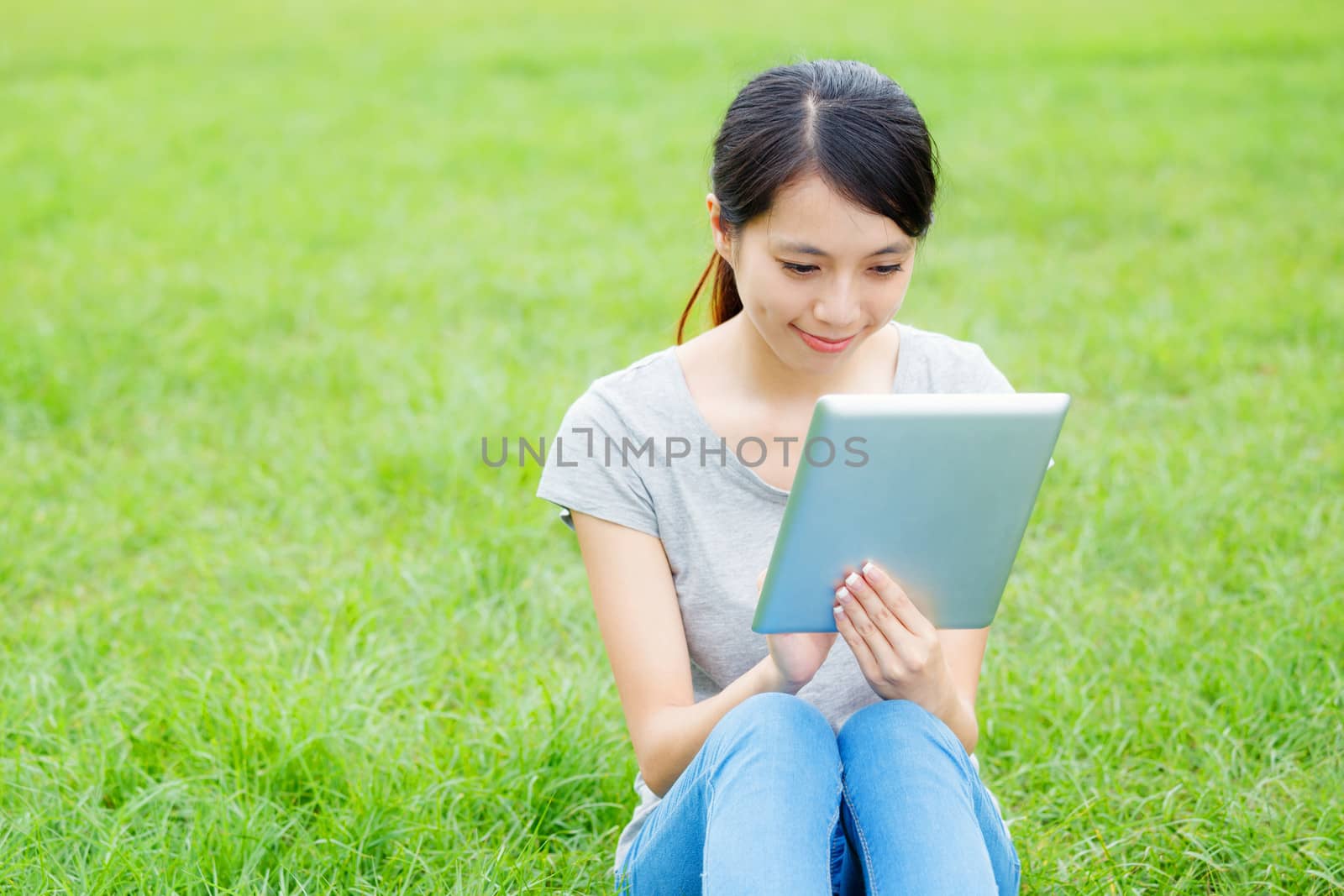 Woman sitting on grass with tablet computer by leungchopan