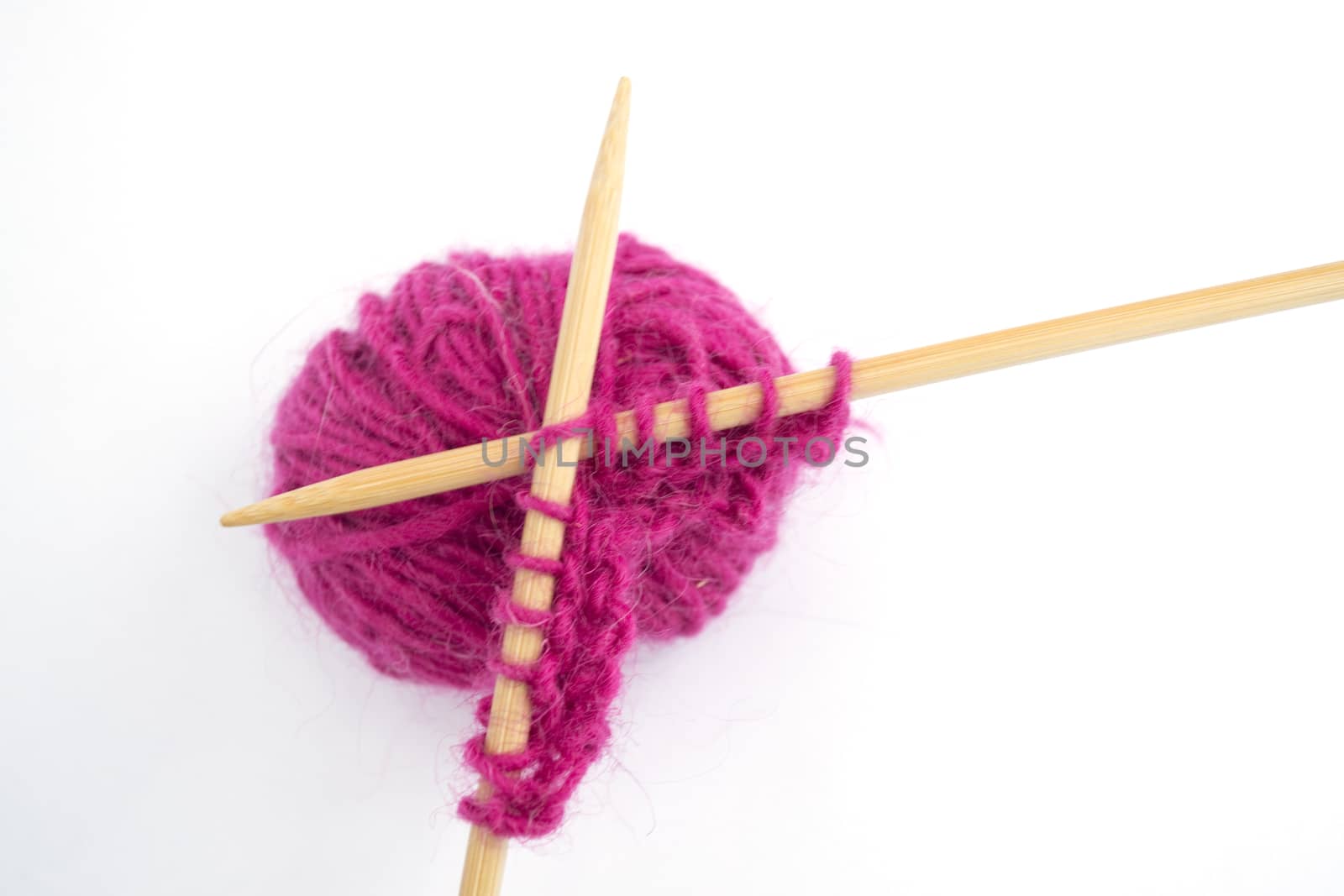 Close up of pink wool around knitting needles on a white background
