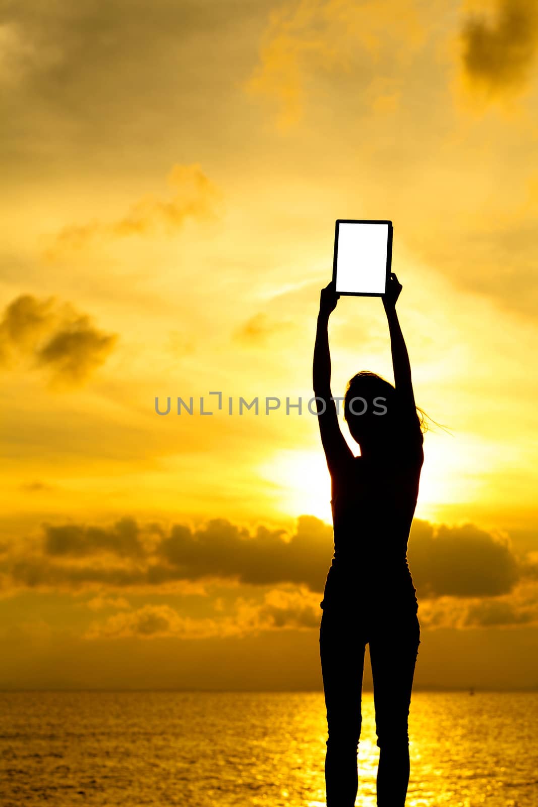 Silhouette of woman holding tablet computer at sunset