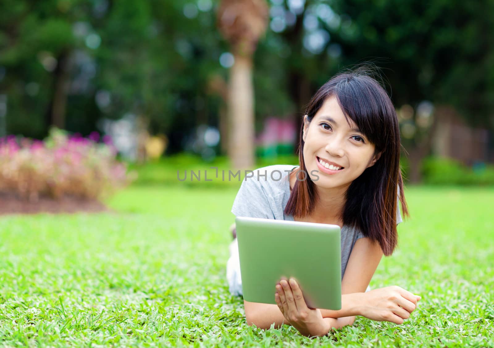 Woman lying on grass with tablet computer by leungchopan