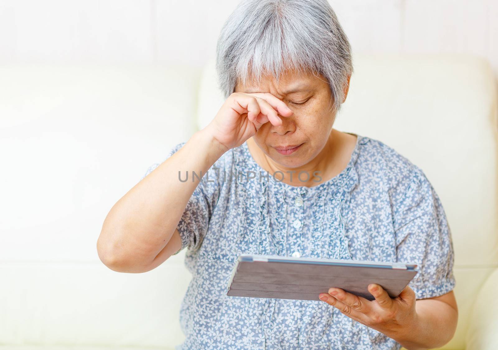 Asian old woman using digital tablet with tired eyes