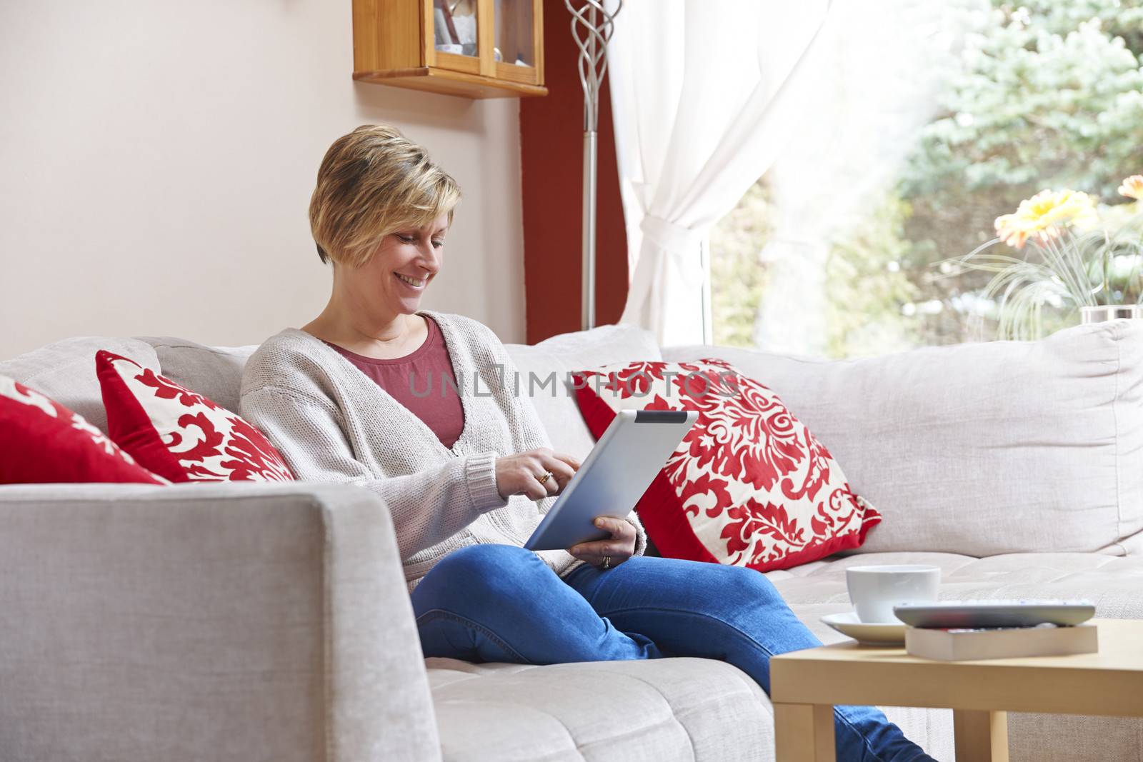 Mother enjoying surfing on the net with tablet  while relaxing at home with coffee