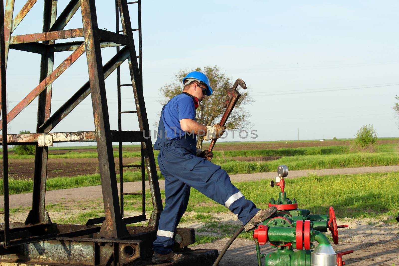 worker with pipe wrench on oilfield pipeline by goce