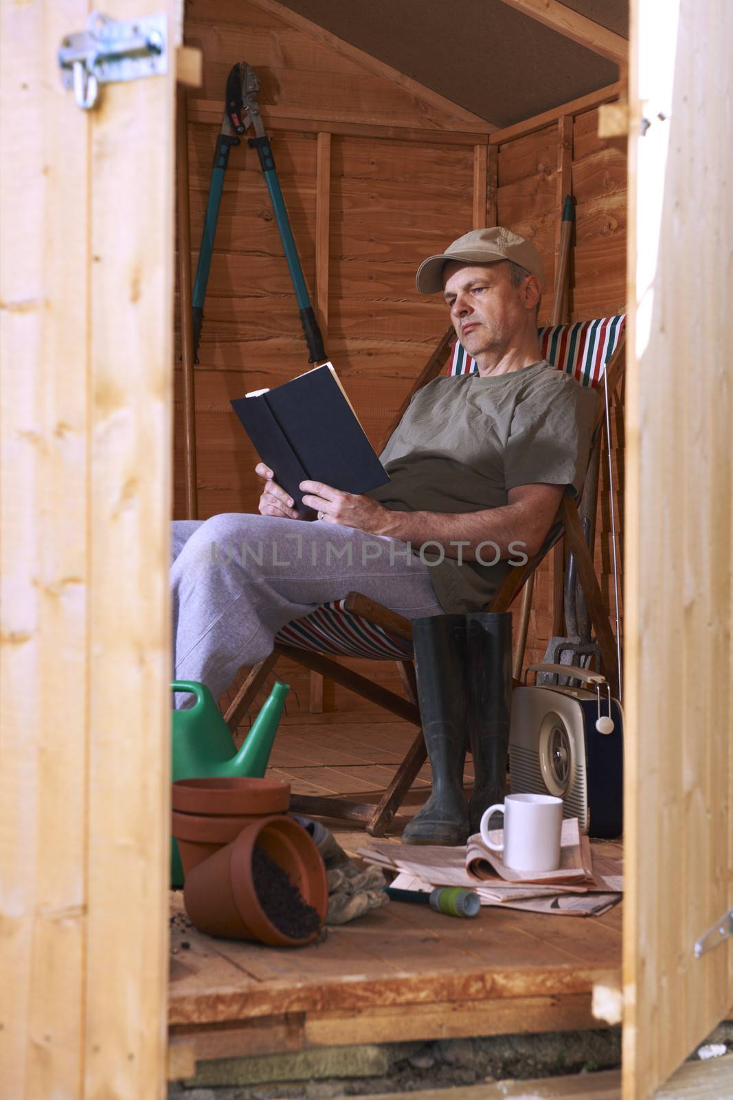 Man reading book while sitting in deckchair in his garden shed