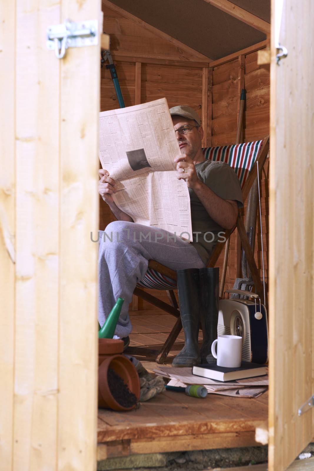 Man checking share prices while sitting in deckchair in his garden shed