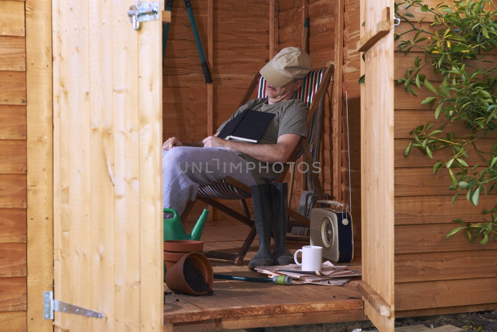 Man sitting in deckchair falling asleep in the shed while reading book