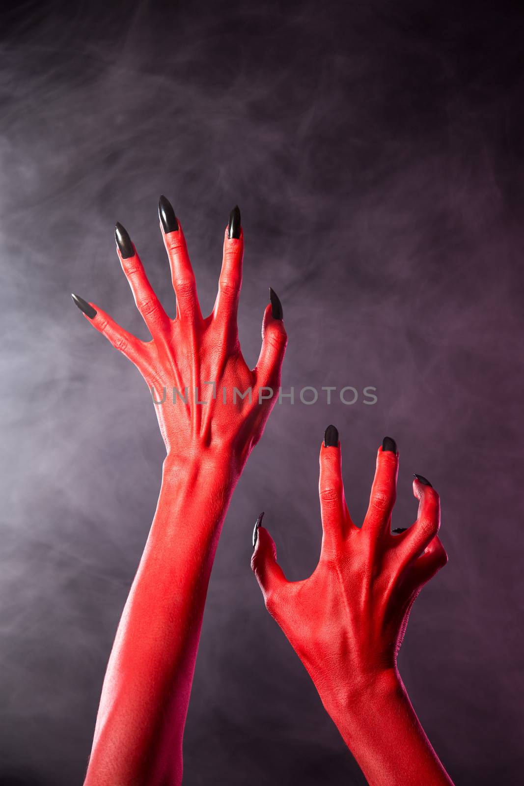 Red devil hands with black nails, Halloween theme, studio shot over smoky background 