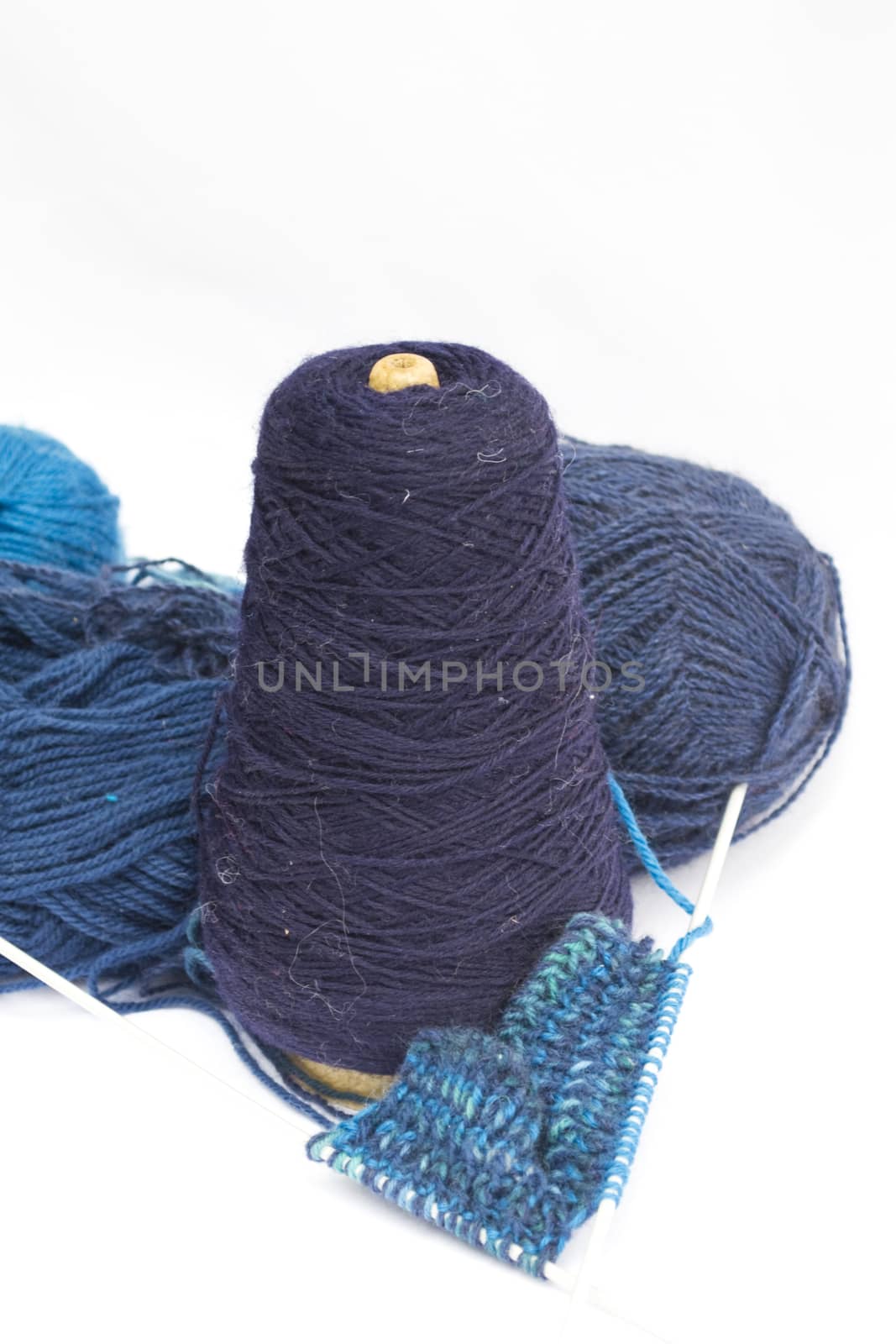 Cone of blue wool with knitting needles on a white background
