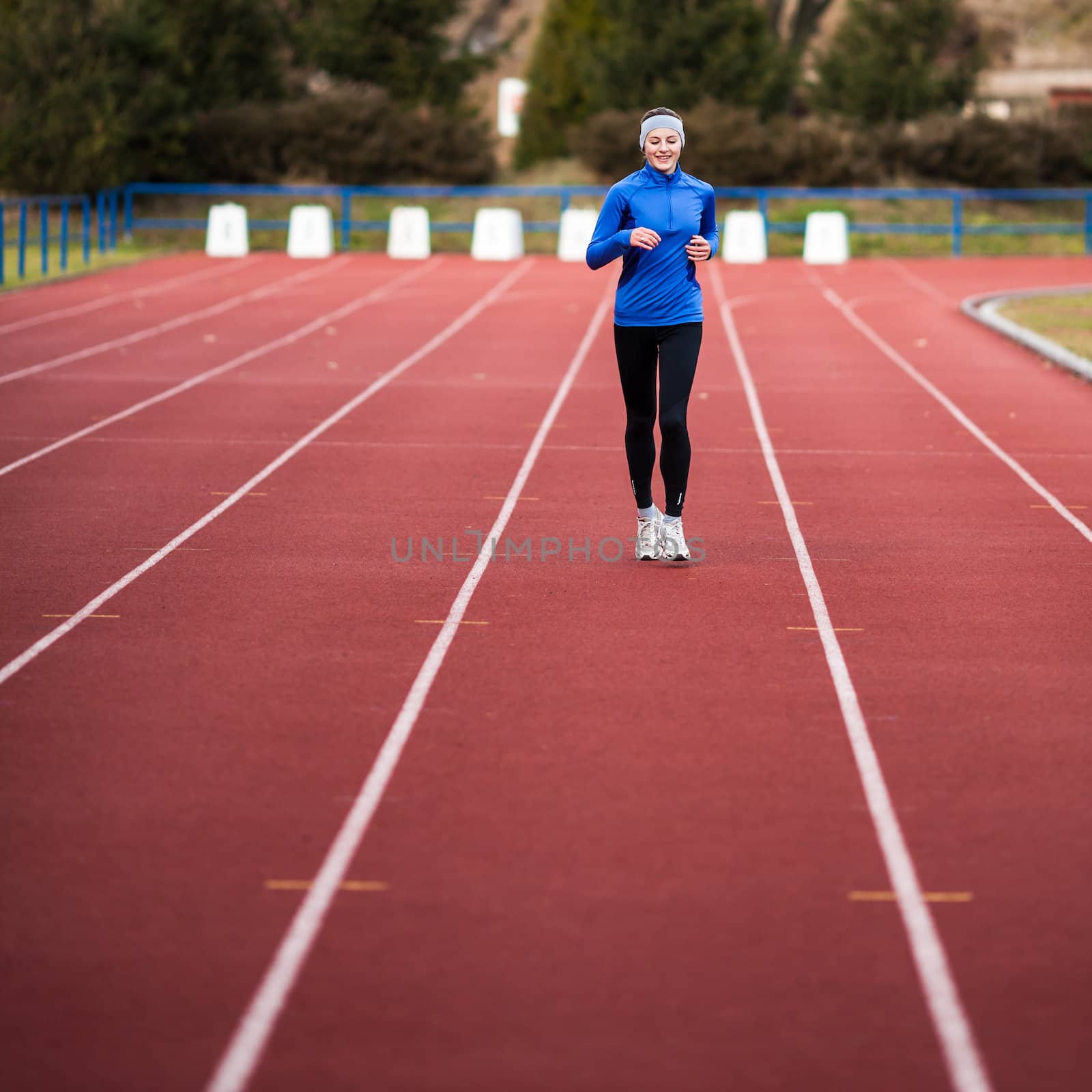 Young woman running at a track and field stadium by viktor_cap