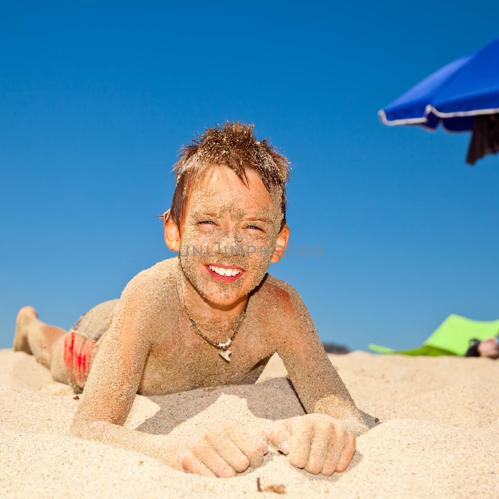 Happy boy covered with sand on a beach