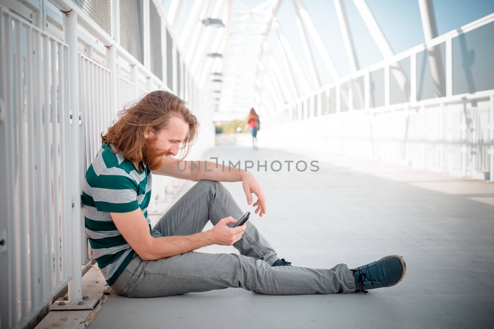 stylish hipster model with long red hair and beard lifestyle on the phone in the street