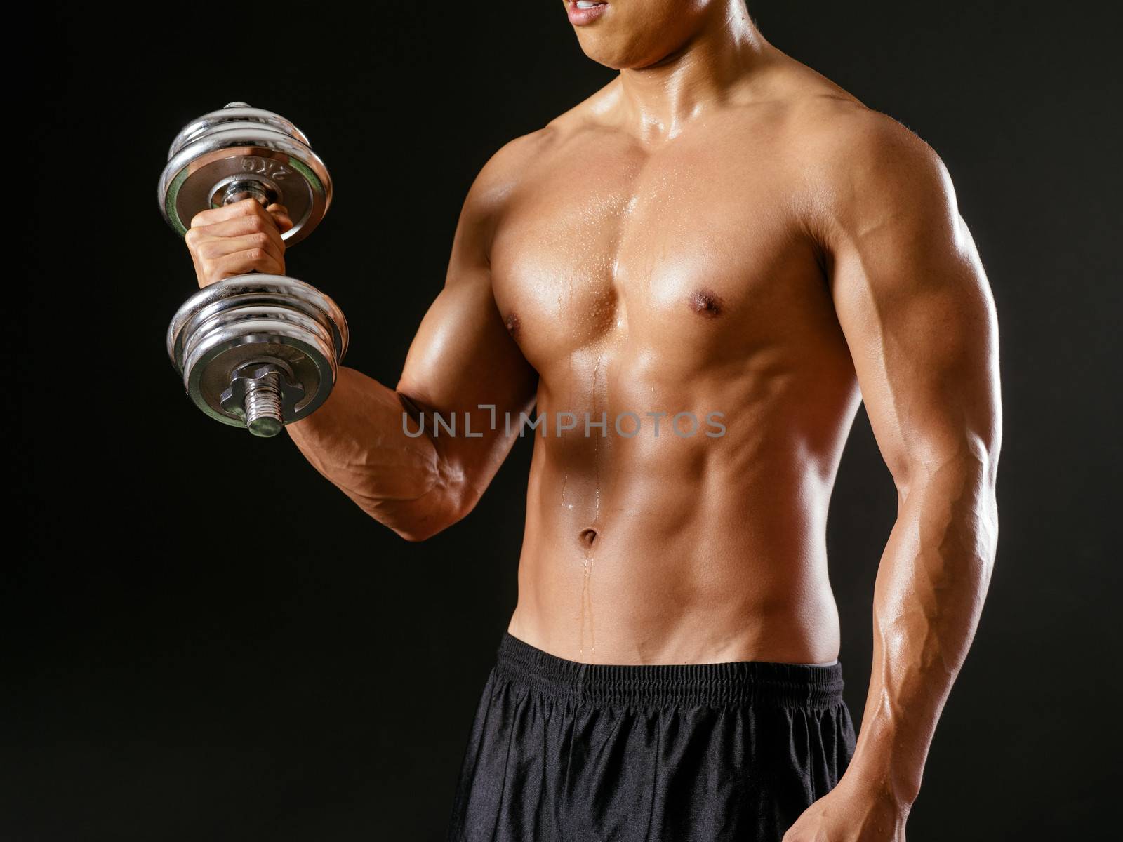 Photo of an Asian male exercising with dumbbells and doing bicep curls over dark background.