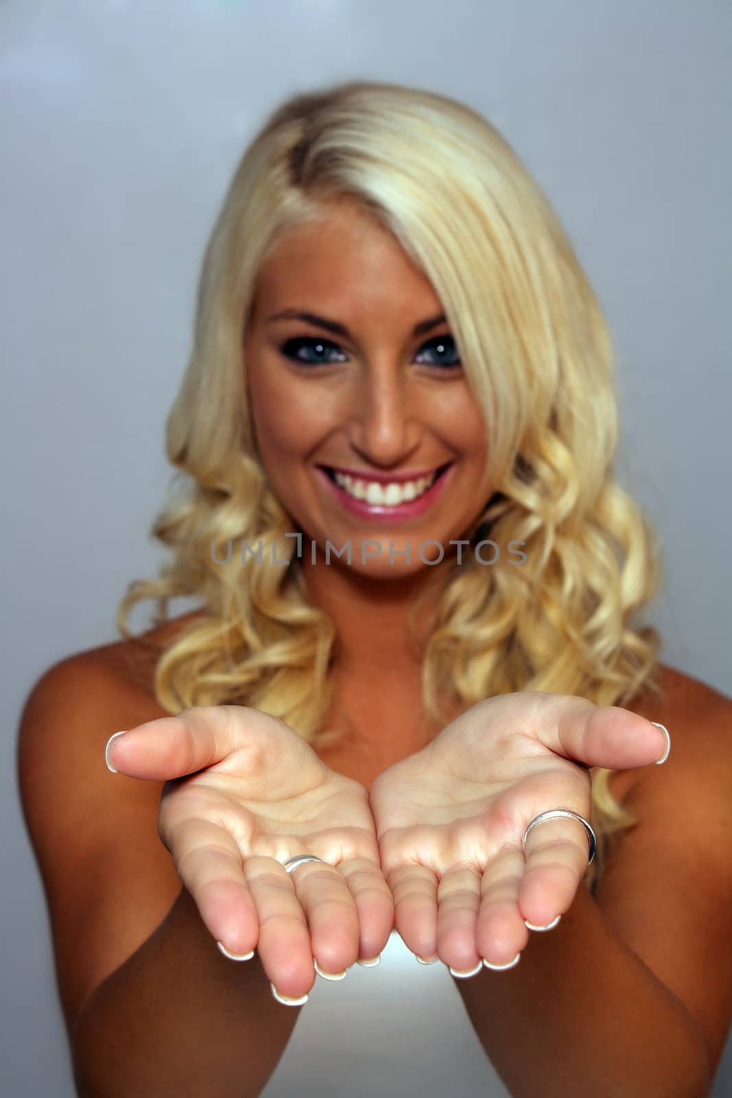 An extraordinarily beautiful young blonde with a bright, warm smile and her hands extended to allow you to put your text or graphic in them.  Selective focus on hands.