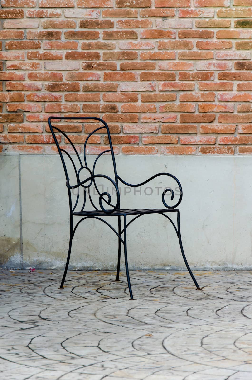 Black iron chair behind a brick wall.