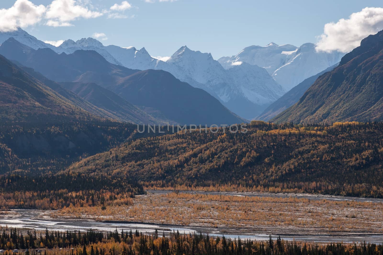Rugged snow capped peaks rise above autumn lowlands