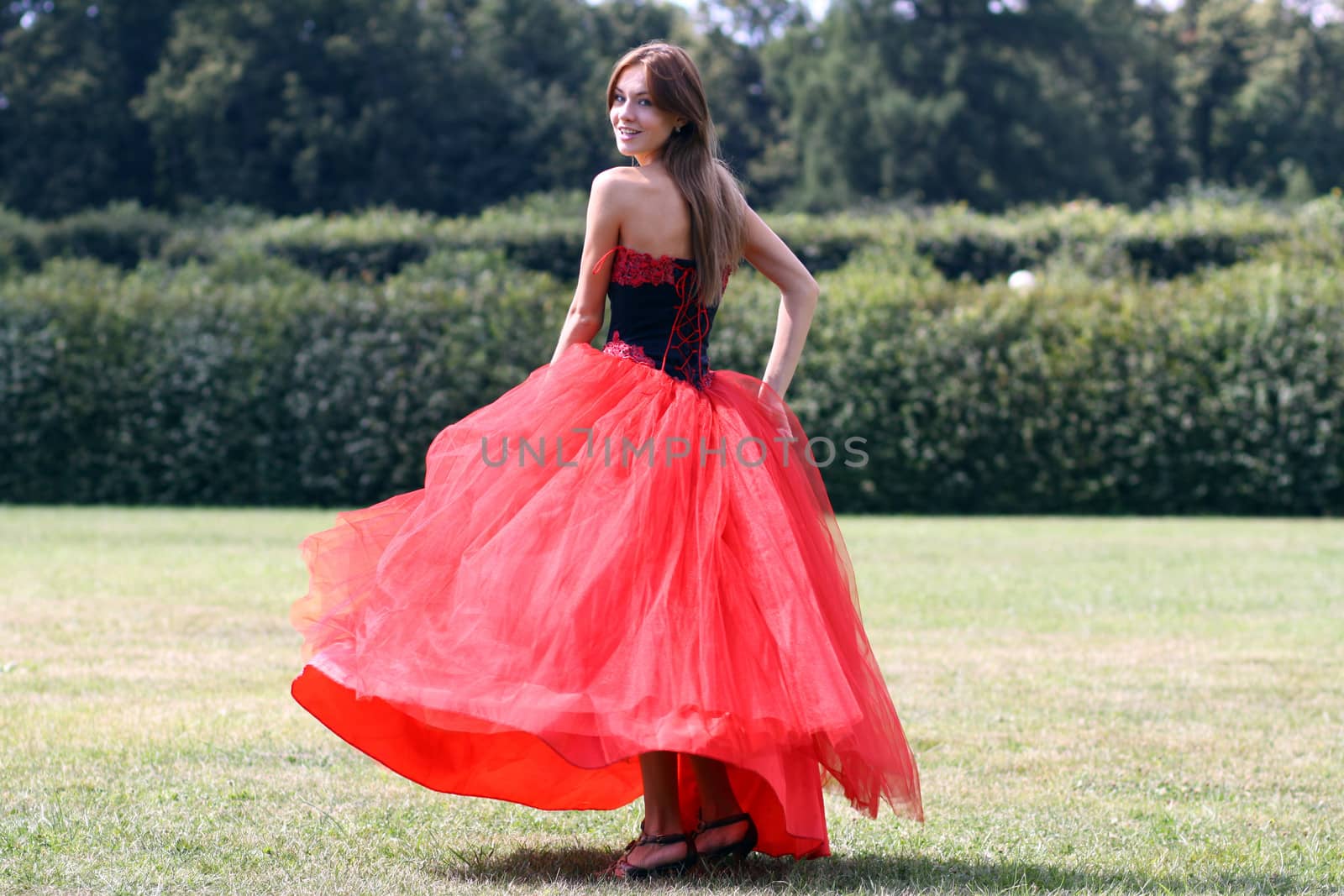 Beautiful woman in a red dress walking on meadow in park