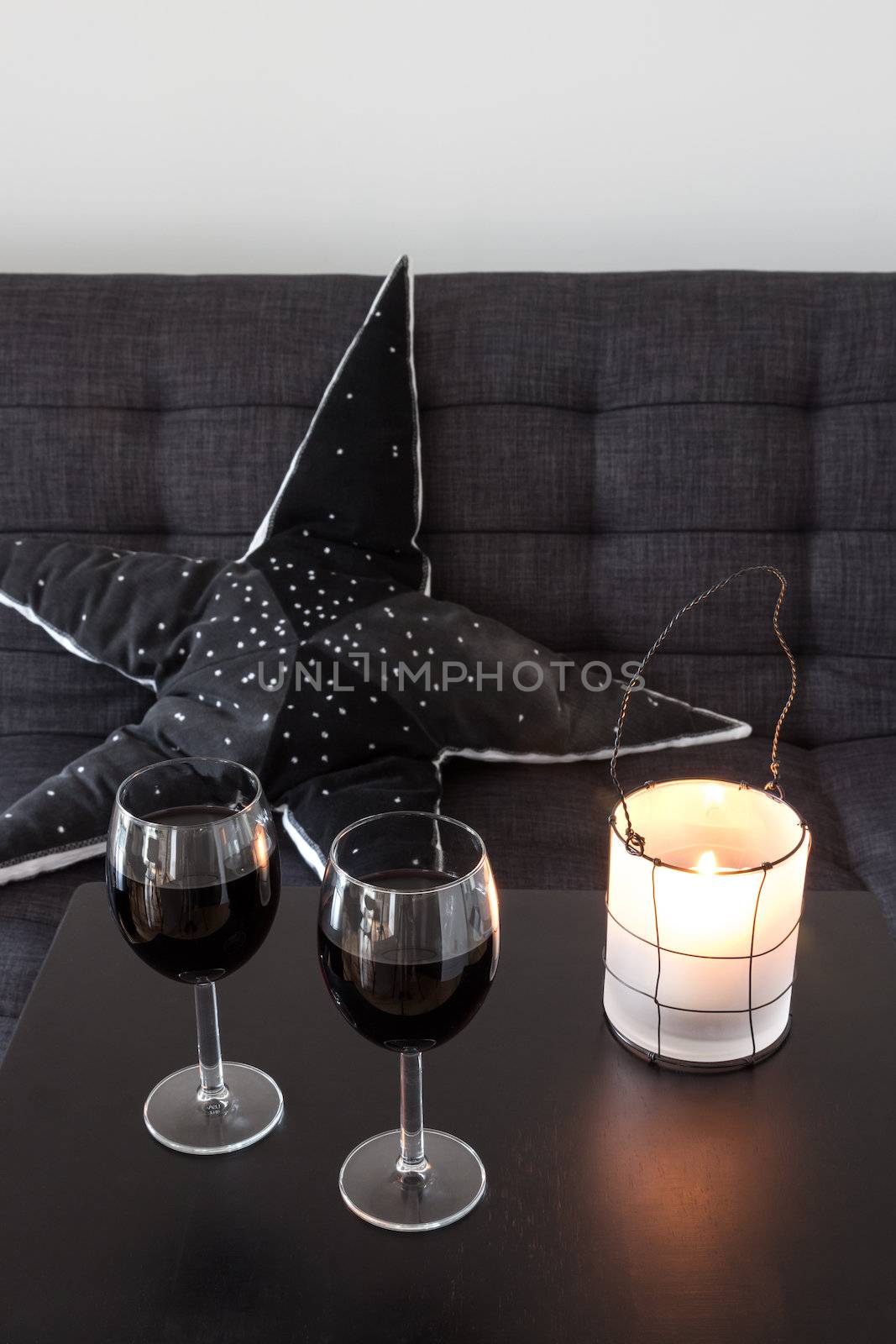 Sofa with decorative cushion, lantern and wineglasses on the table.