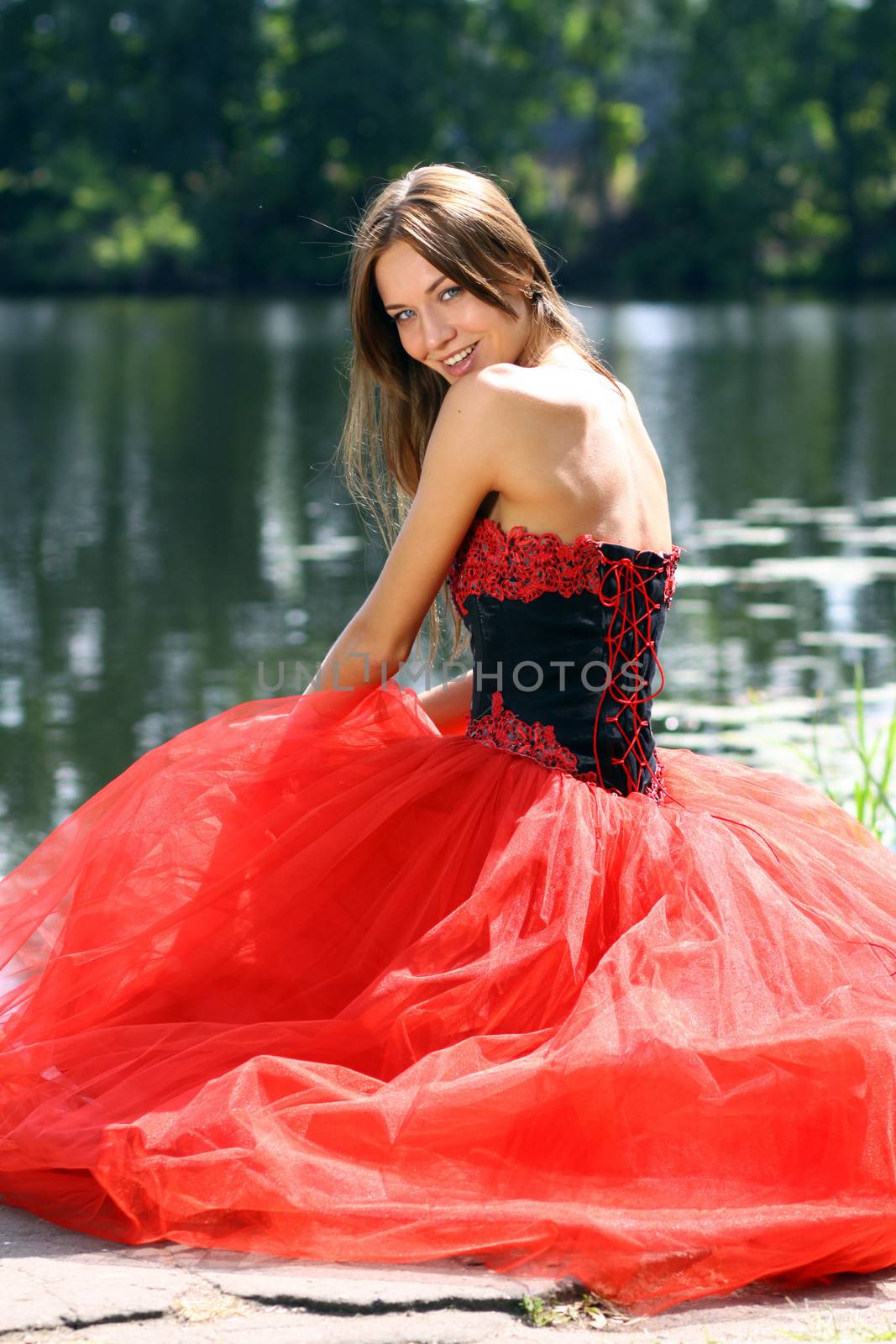 Smiling woman in a red dress sitting near river