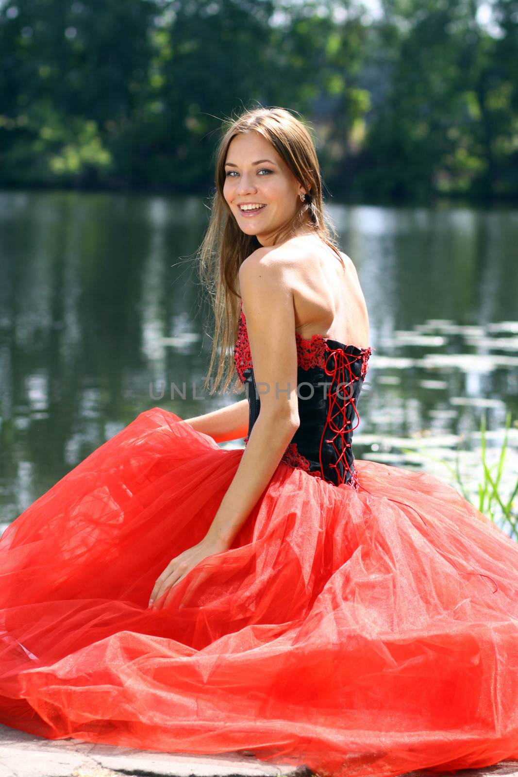 Smiling woman in a red dress sitting near river